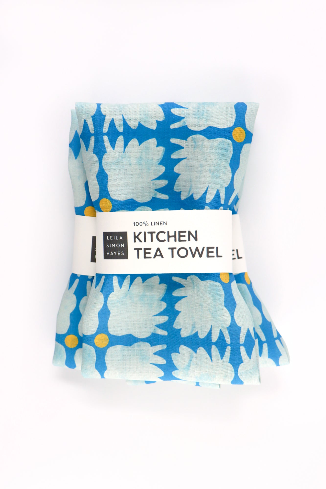 Packaged kitchen tea towel with blue floral pattern on a white background. Designed by artist Leila Simon Hayes.