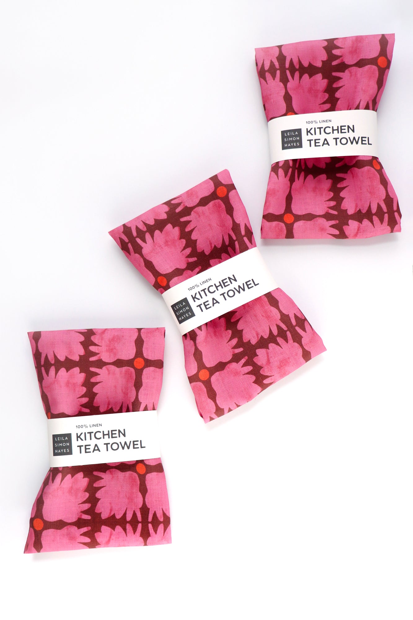 Set of four pink patterned kitchen tea towels on a white background. Designed by artist Leila Simon Hayes.
