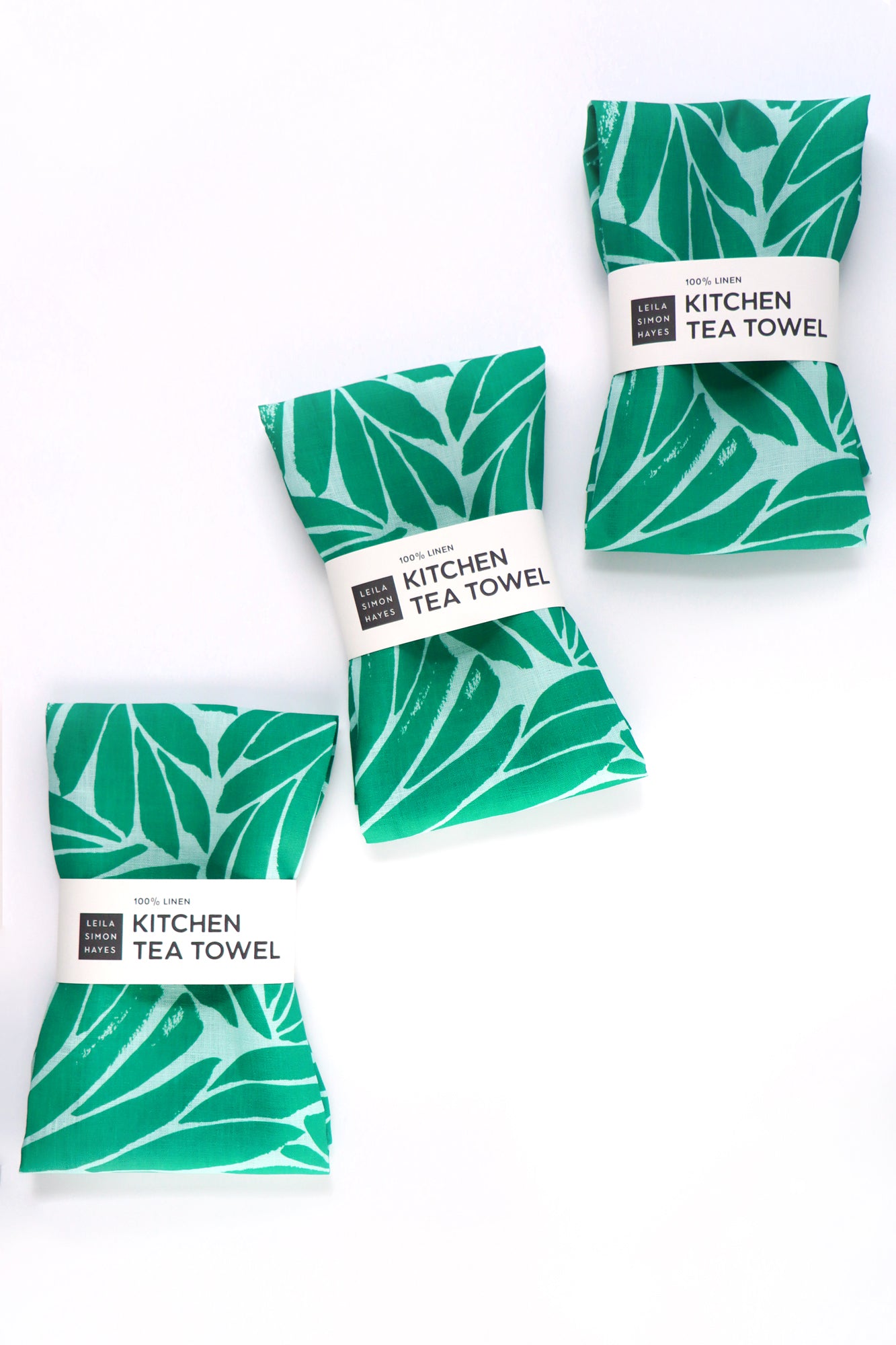 Set of three green leaf-patterned kitchen tea towels on a white background. Designed by artist Leila Simon Hayes.