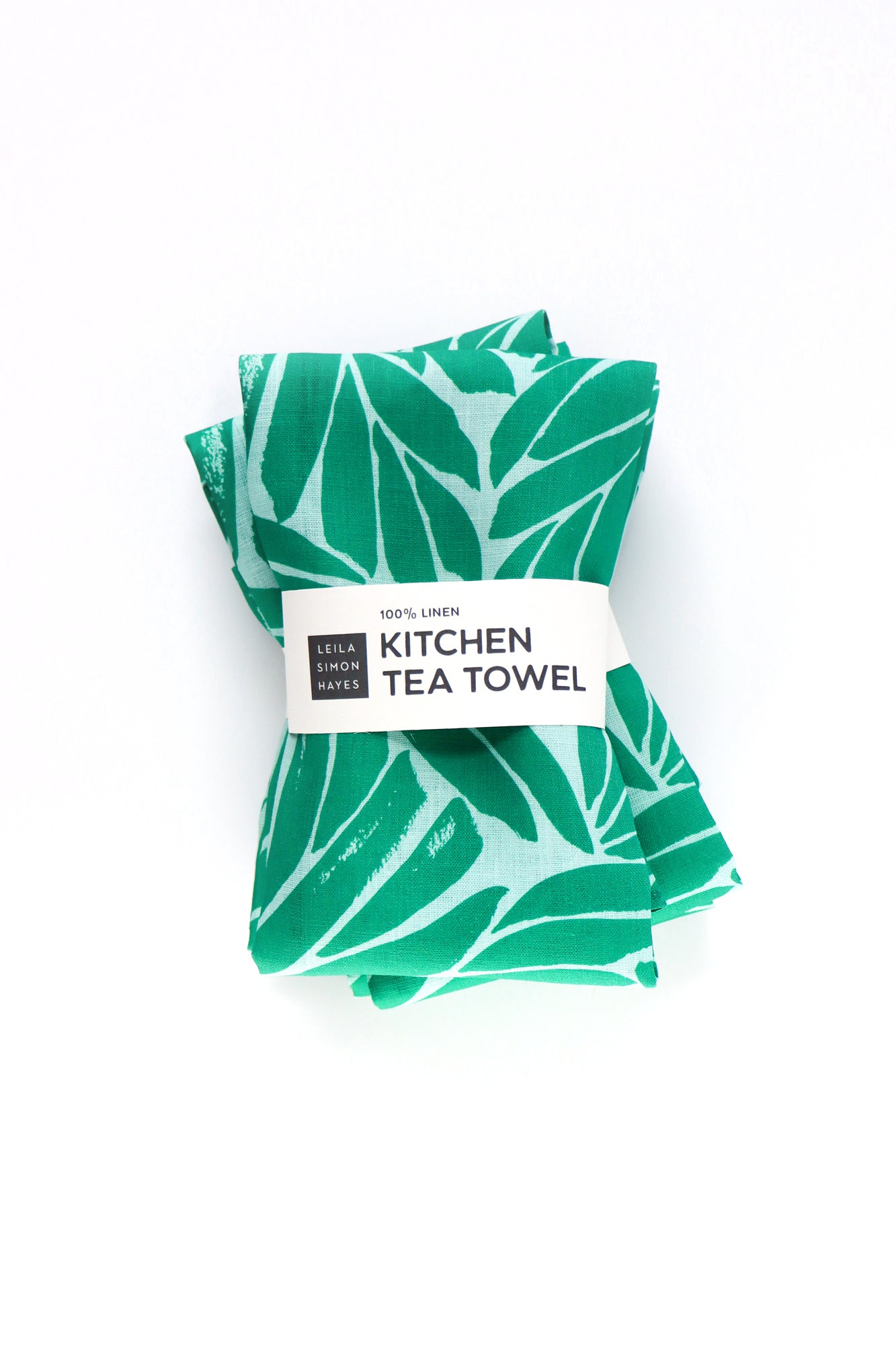 Green leaf-patterned kitchen tea towel with a label on a white background. Designed by artist Leila Simon Hayes.