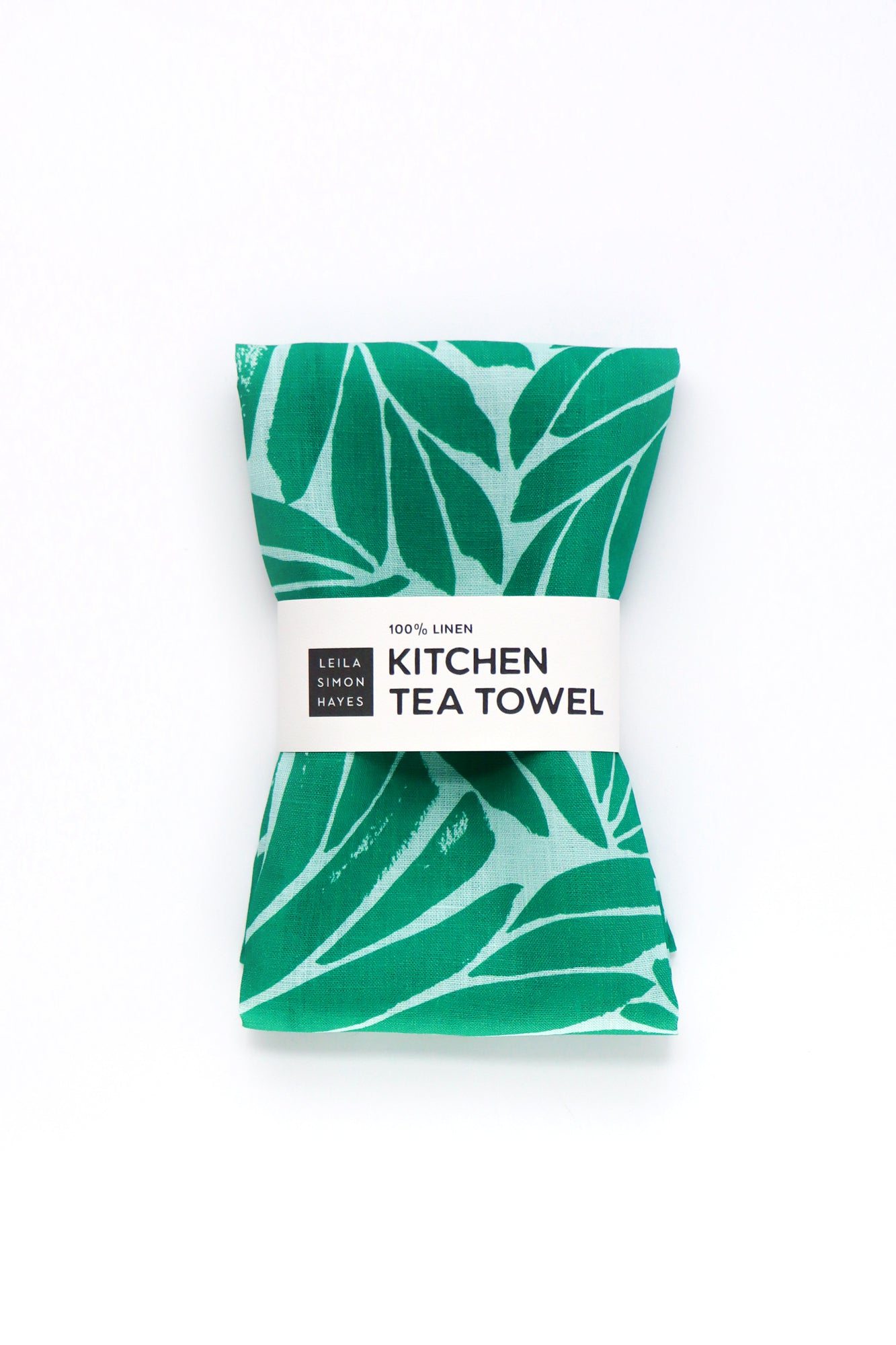 Green leaf-patterned kitchen tea towel with a label on a white background. Designed by artist Leila Simon Hayes.