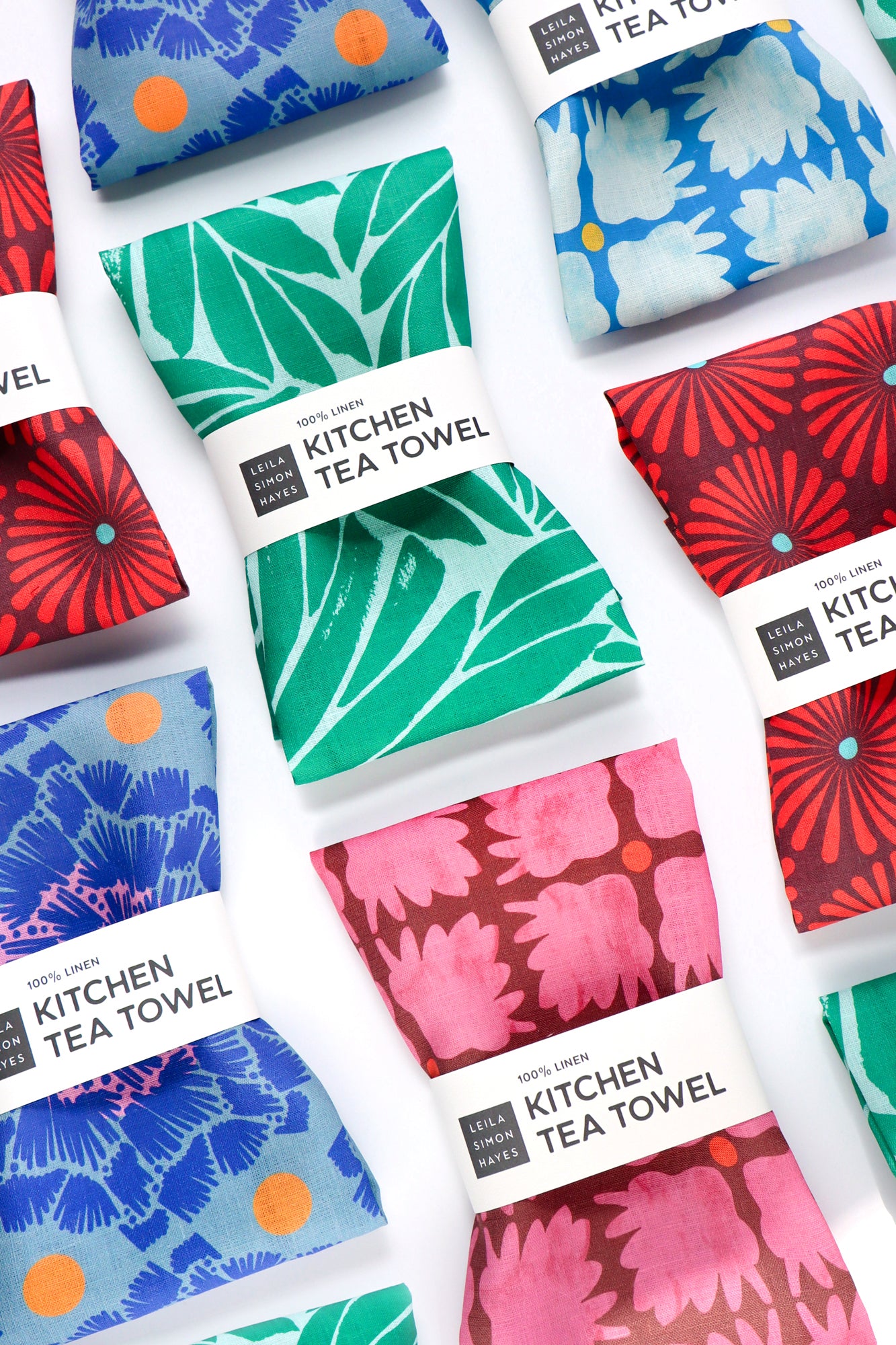 Collection of colorful kitchen tea towels with various patterns on a white background. Designed by artist Leila Simon Hayes.