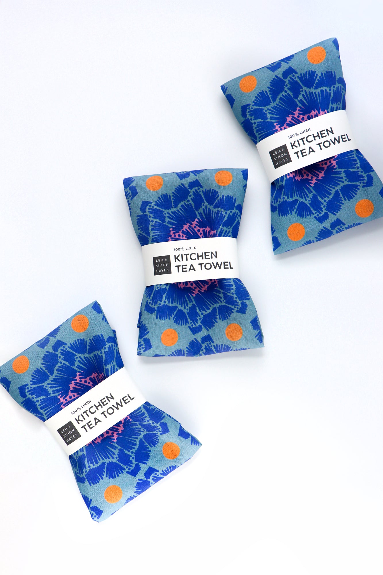 Three blue kitchen tea towels with orange dots on a white background. Designed by artist Leila Simon Hayes.