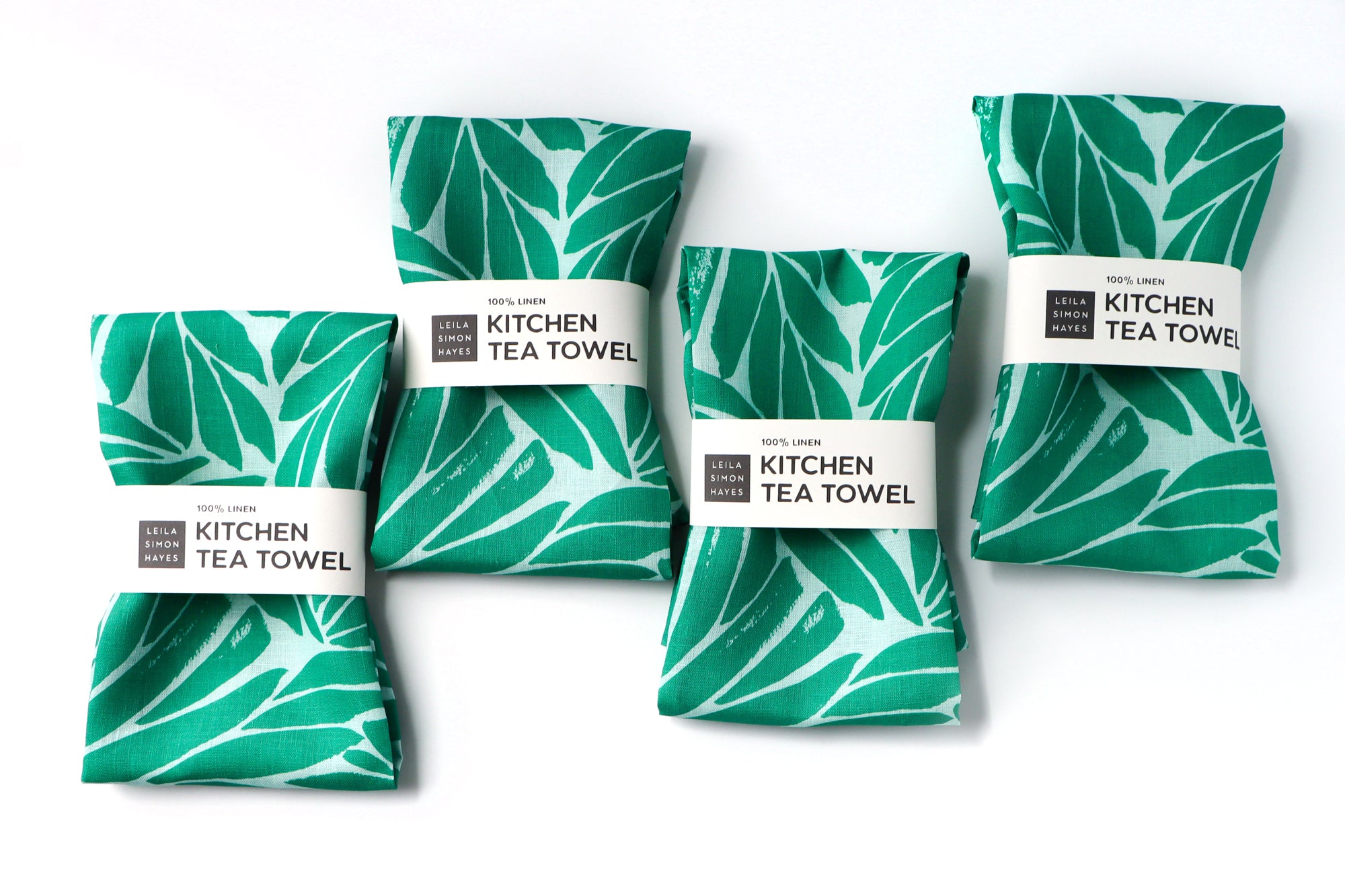 Four green kitchen tea towels with leaf patterns on a white background. Designed by artist Leila Simon Hayes.