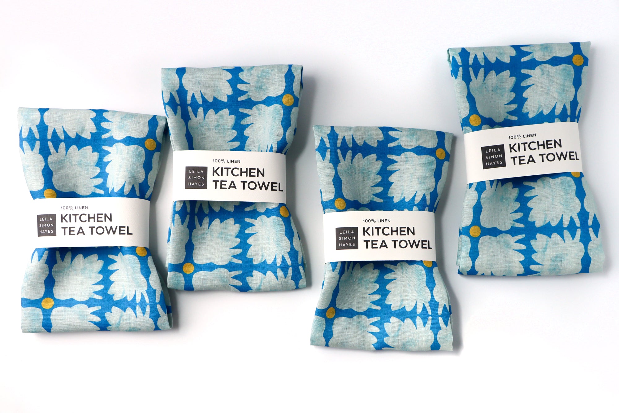 Four blue and white patterned kitchen tea towels with labels on a white background. Designed by artist Leila Simon Hayes.
