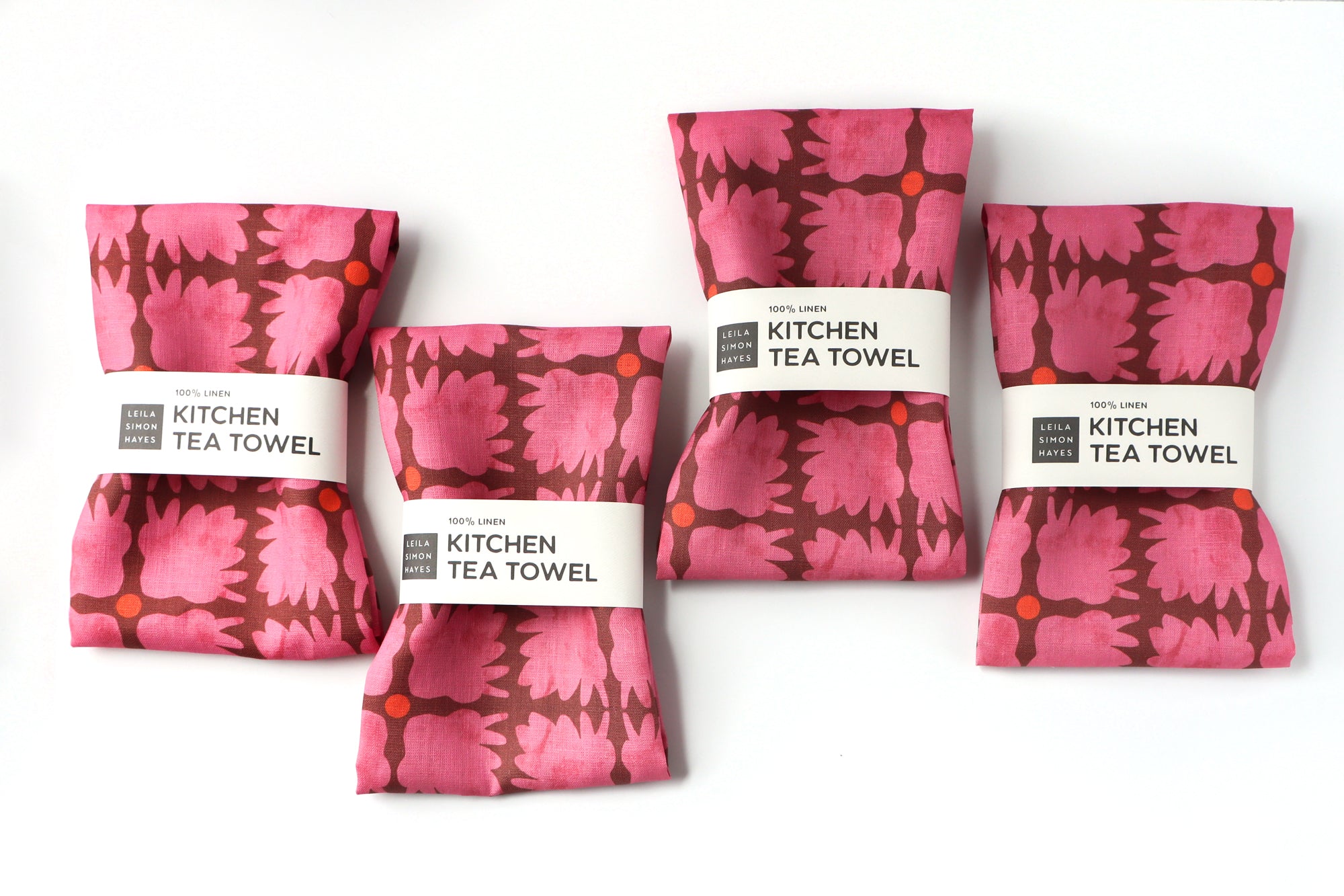 Set of pink patterned kitchen tea towels with labels on a white background. Designed by artist Leila Simon Hayes.