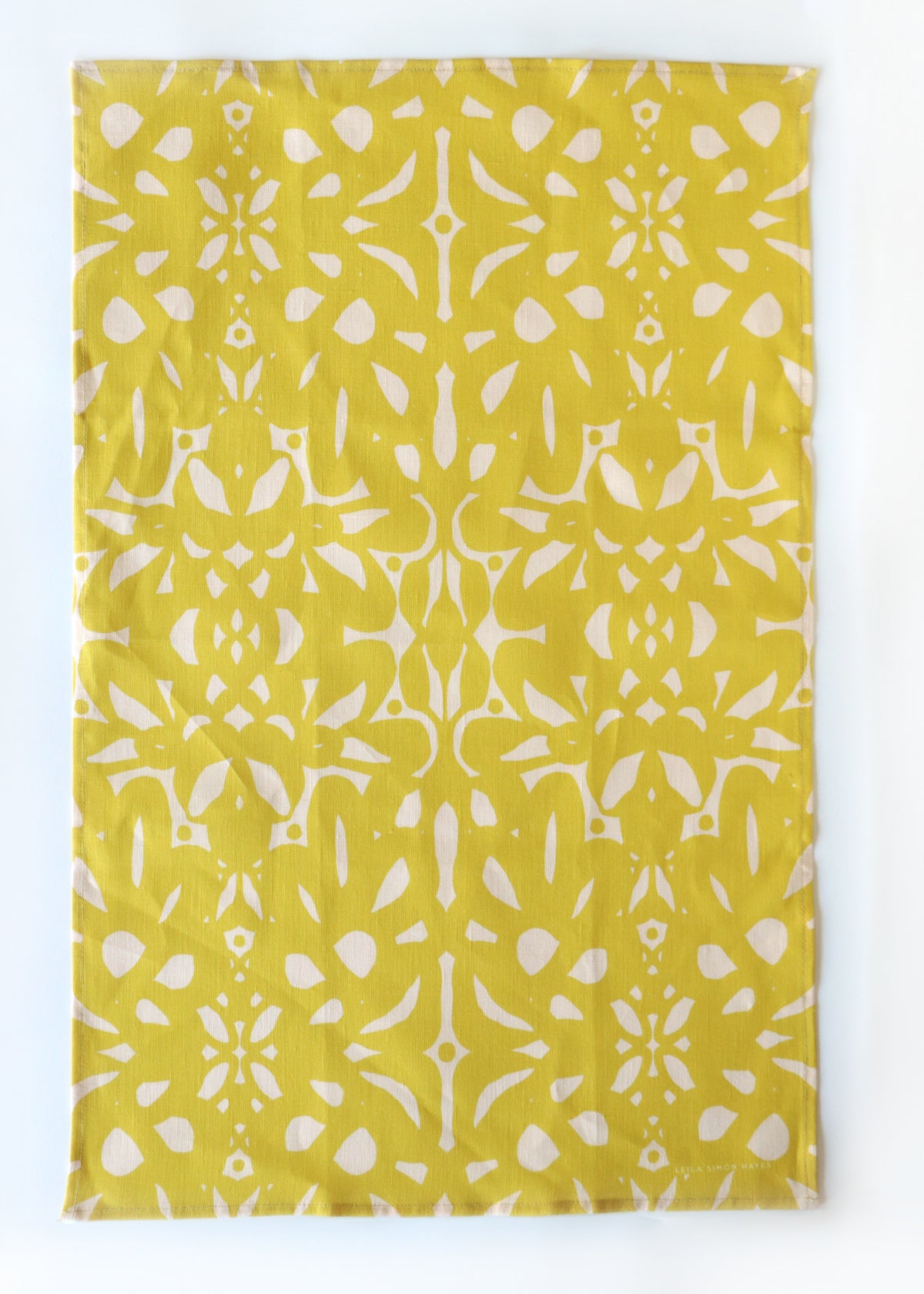Yellow tea towel with white geometric pattern on a white background. Designed by artist Leila Simon Hayes.