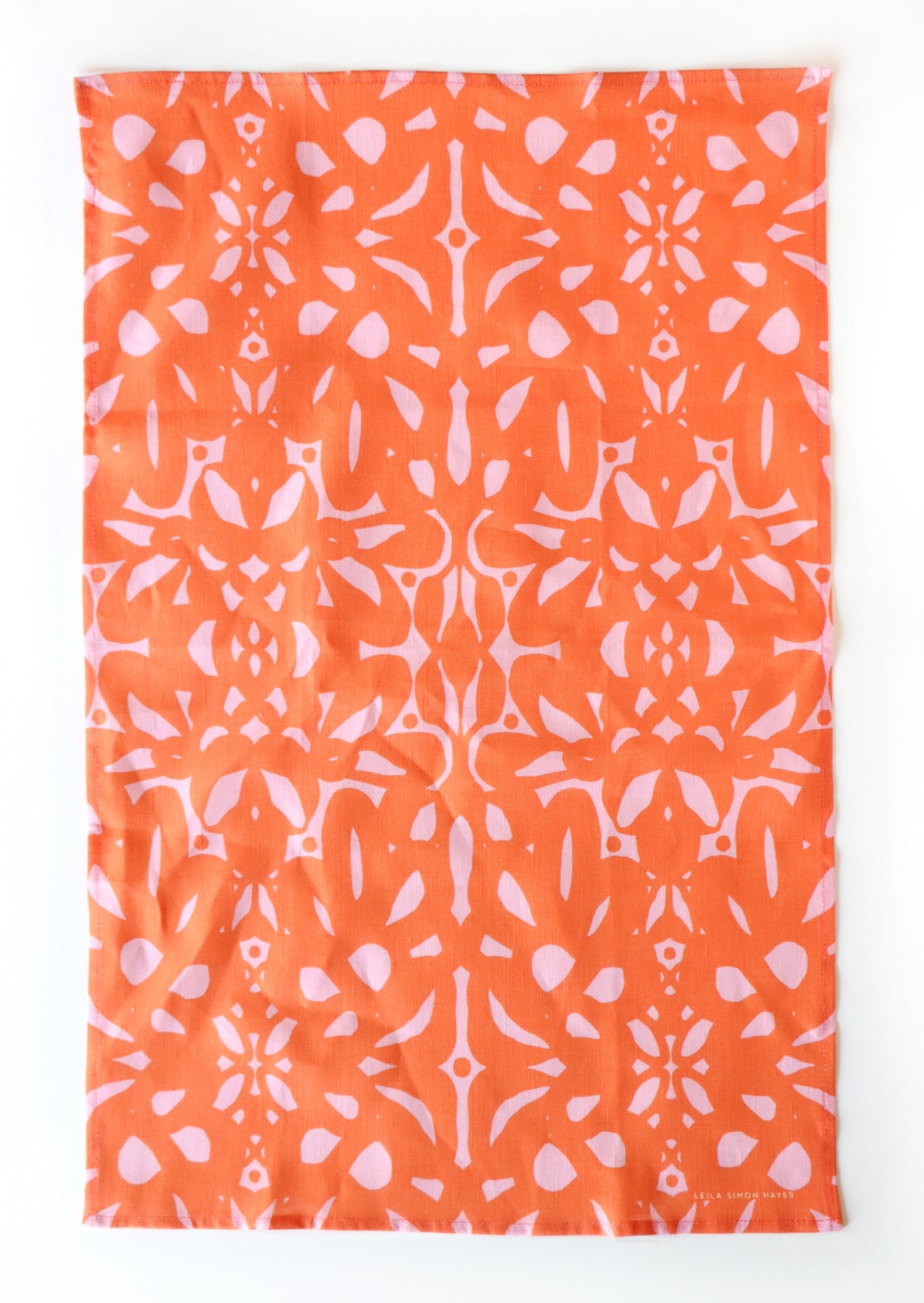 Orange tea towel with white abstract pattern on a white background. Designed by artist Leila Simon Hayes.