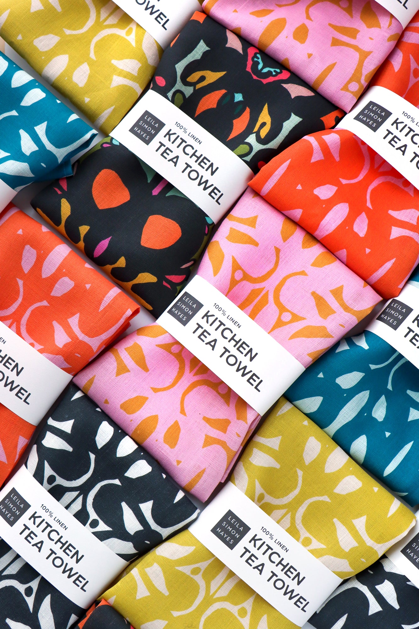 Collection of colorful kitchen tea towels with various patterns and labels. Designed by artist Leila Simon Hayes.