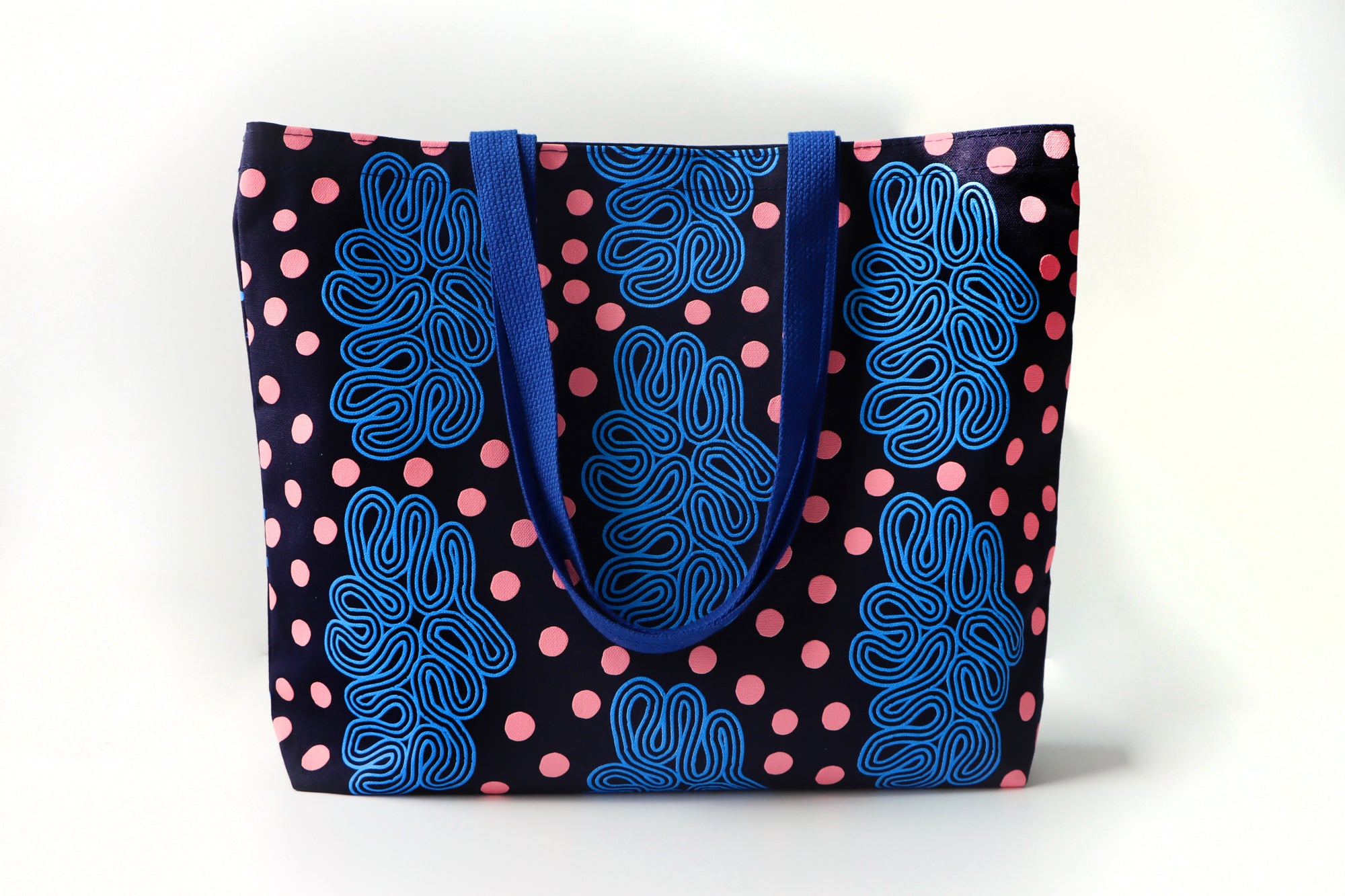 Tote bag with blue loops pattern and pink dots on a white background. Designed by artist Leila Simon Hayes.