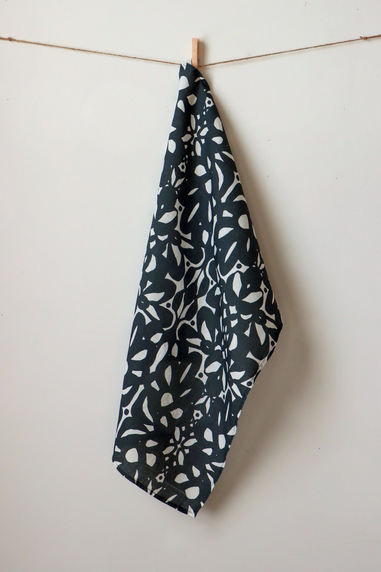 Black and white tea towel with abstract pattern hanging on a clothesline against a white background. Designed by artist Leila Simon Hayes.