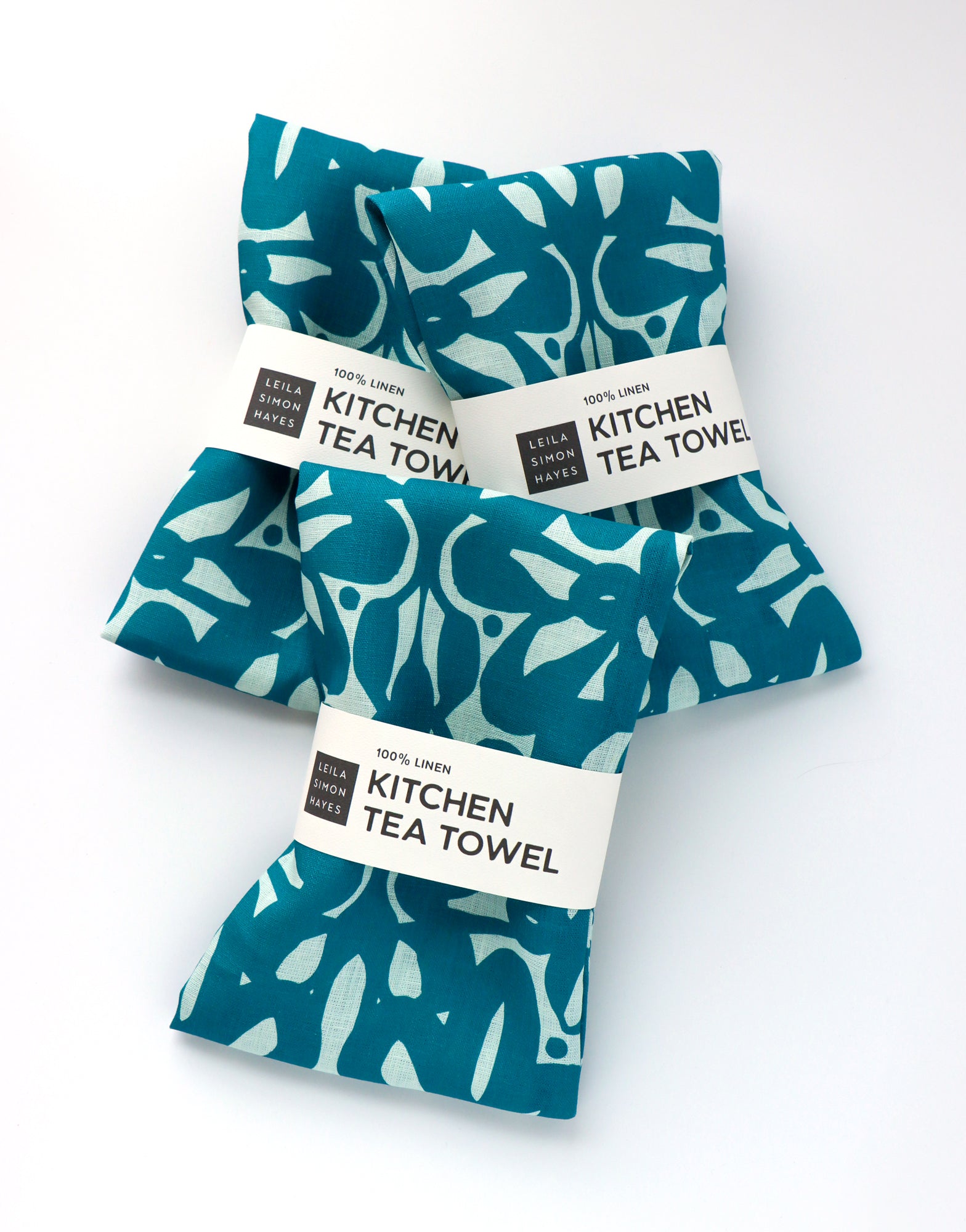 Three blue patterned kitchen tea towels with labels on a white background. Designed by artist Leila Simon Hayes.