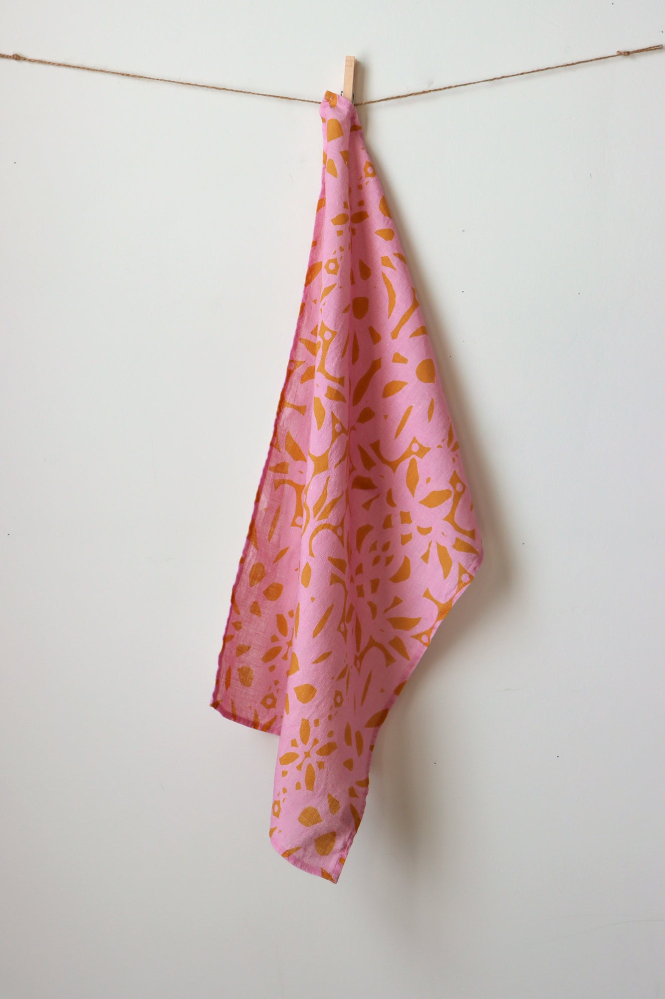 Pink towel with orange pattern hanging on a clothesline against a white wall. Designed by artist Leila Simon Hayes.