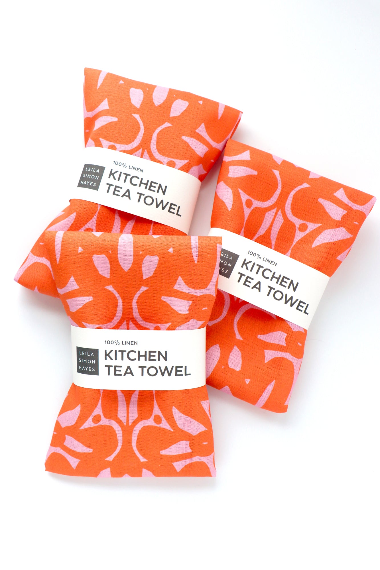 Four orange kitchen tea towels with pink patterns on a white background. Designed by artist Leila Simon Hayes.