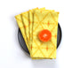 A stack of yellow patterned cloth napkins with a citrus slice on top, arranged on a dark round plate against a clean white background. Designed by artist Leila Simon Hayes. 