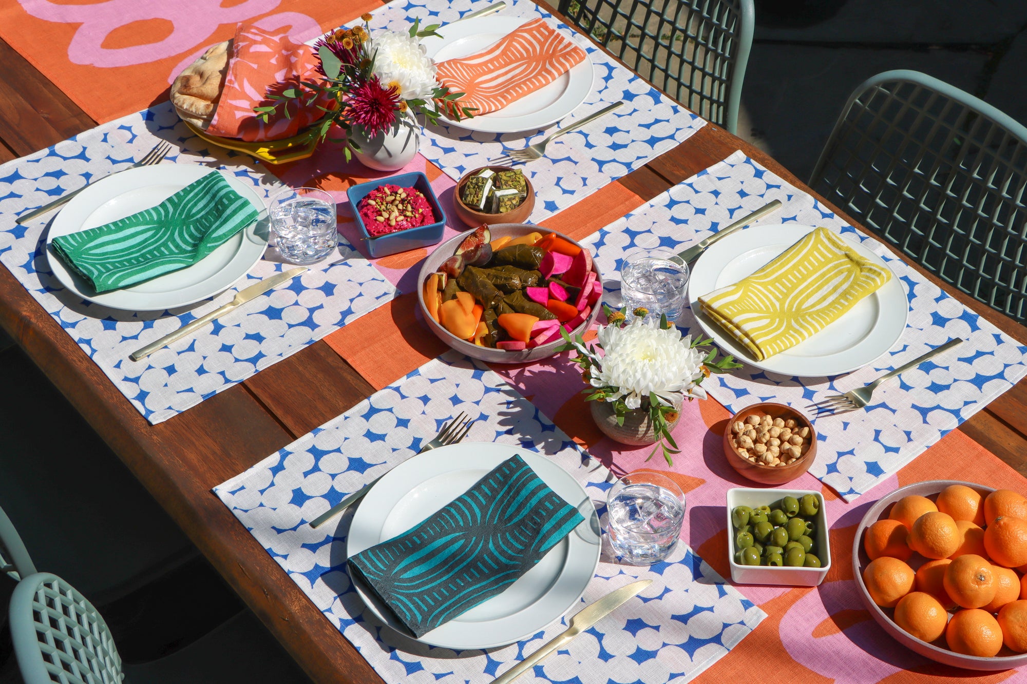 Dining table set with plates, linen napkins, blue and white dotted placemats, on a colorful coral and pink table runner. Designed by artist Leila Simon Hayes