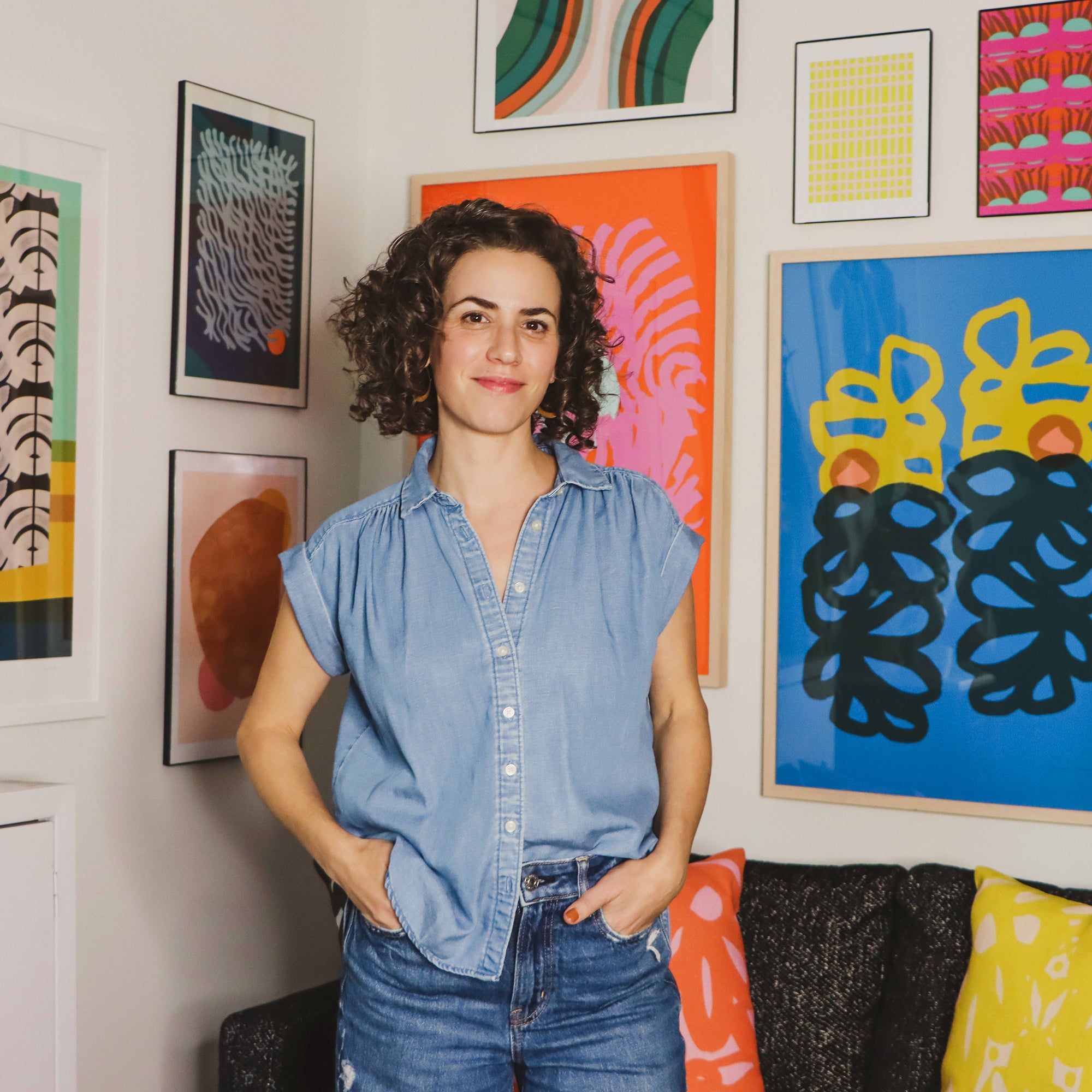 Artist Leila Simon Hayes in her studio with her abstract art prints framed and hung up on a wall in the background.