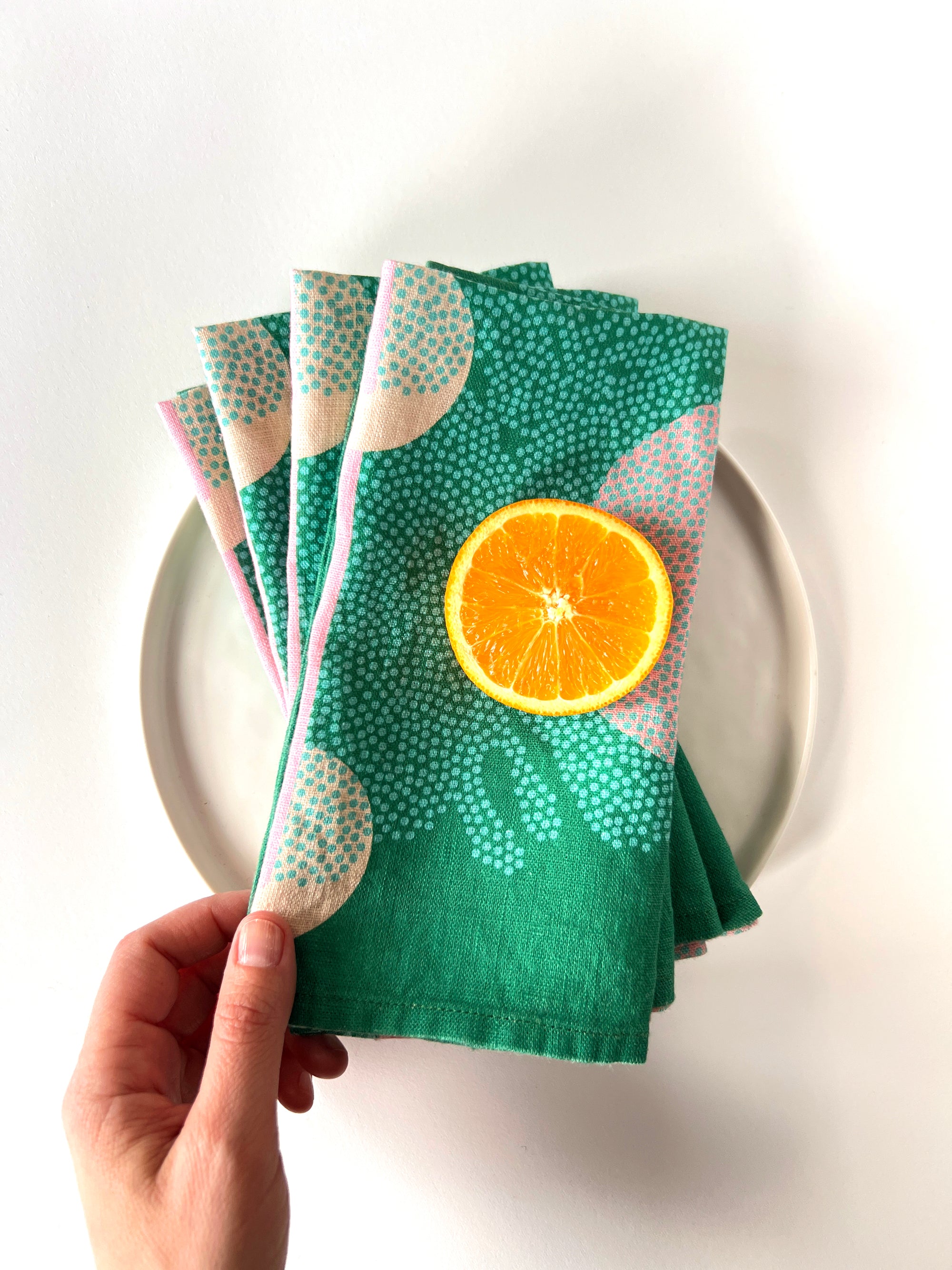 Four green patterned napkins layered over a white plate. Designed by artist Leila Simon Hayes. 