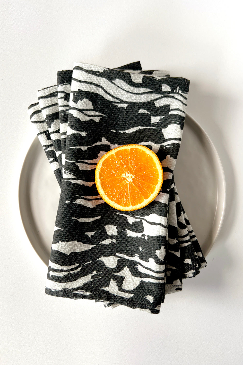 Four black and white patterned napkin with an wave pattern layered on a white plate. Designed by artist Leila Simon Hayes.