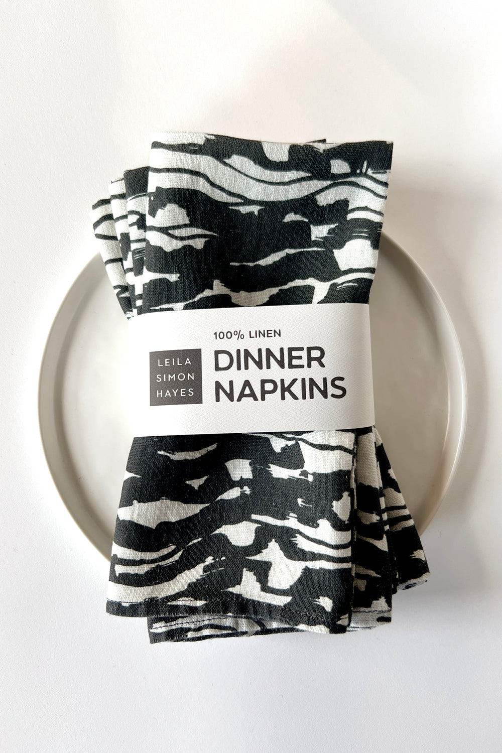 A four pack of black and white wave patterned dinner napkins with a label saying "100% Linen Dinner Napkins", designed by artist Leila Simon Hayes.
