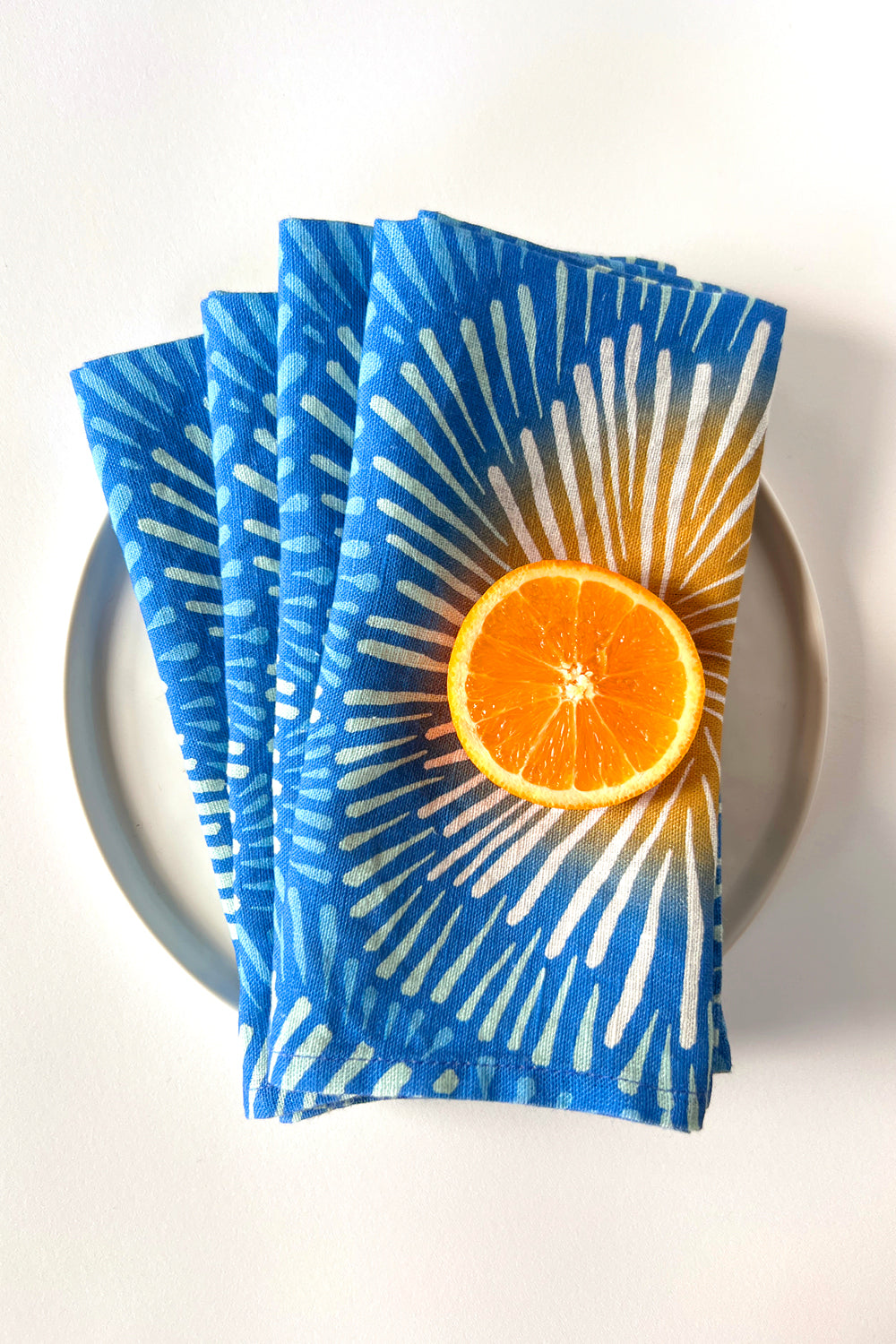 Four blue burst napkins, designed by artist Leila Simon Hayes. All layered on a white plate.