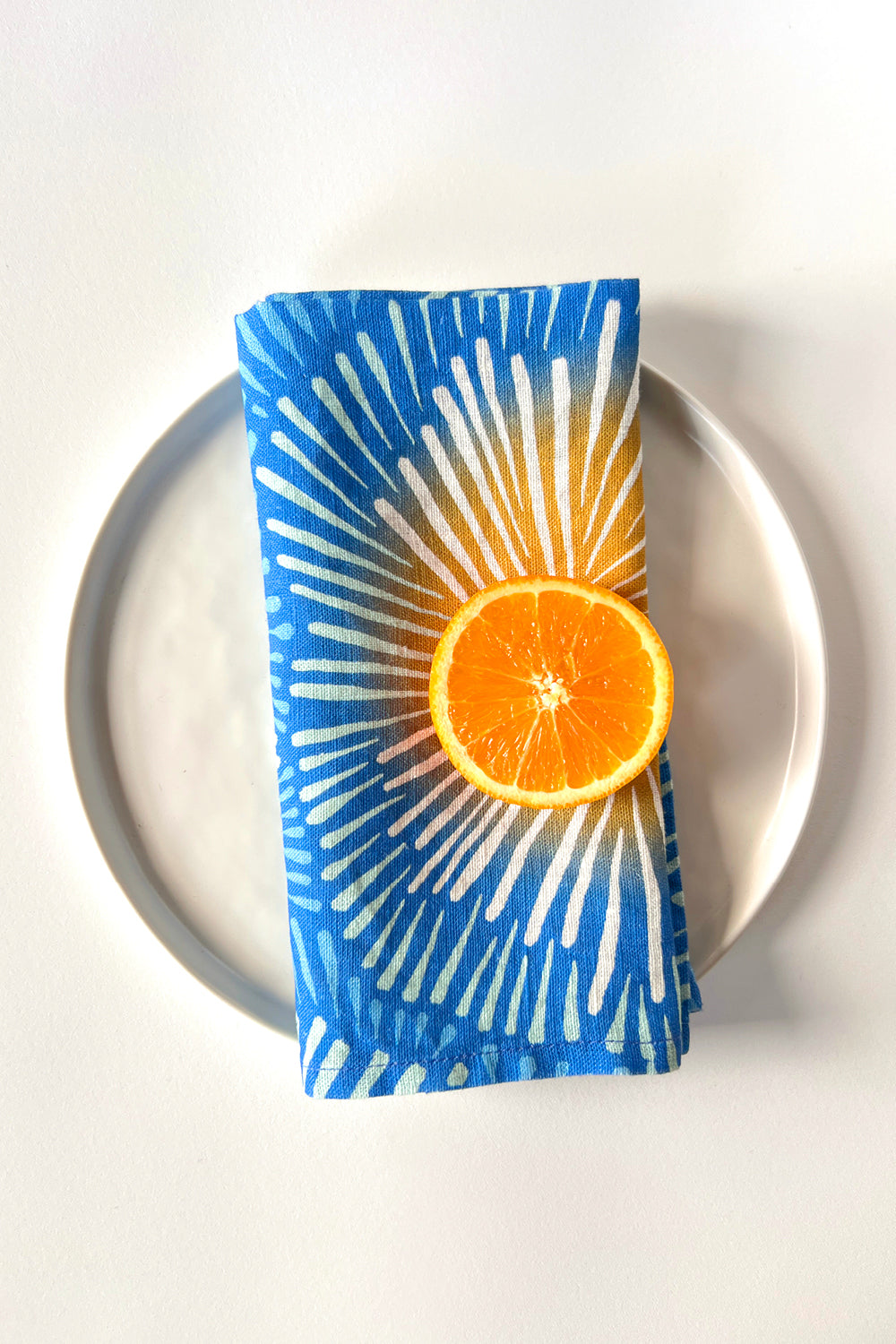 Blue burst napkin, designed by artist Leila Simon Hayes, on a white plate.