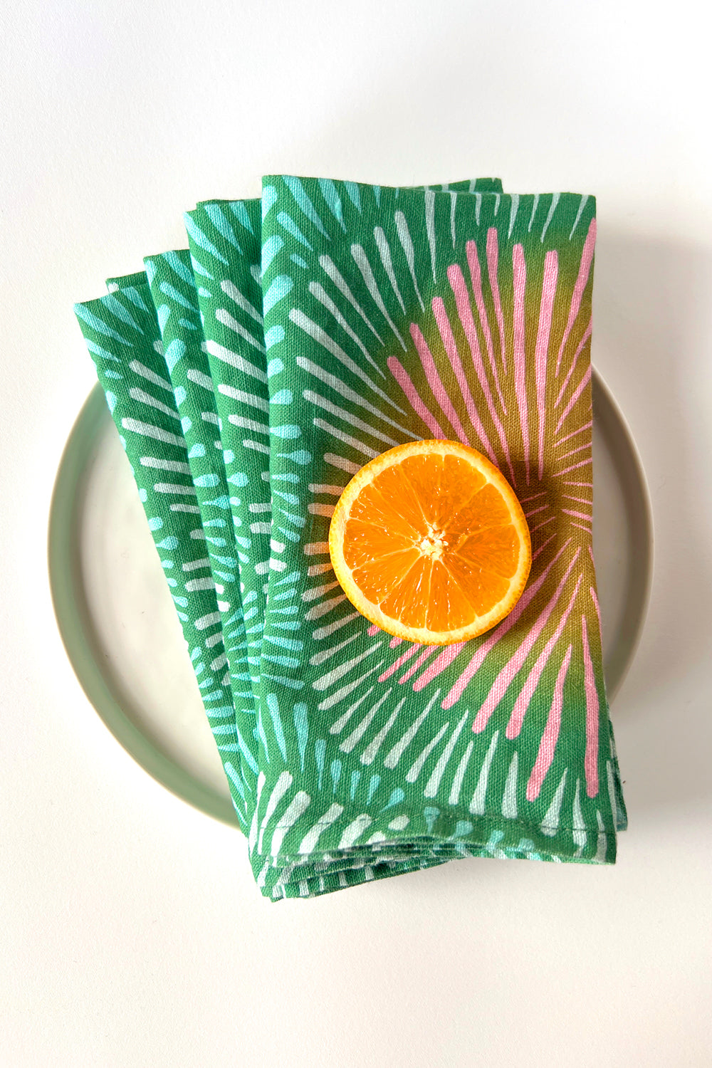 Stack of four green patterned napkins designed by artist Leila Simon Hayes. Layered on a white plate.