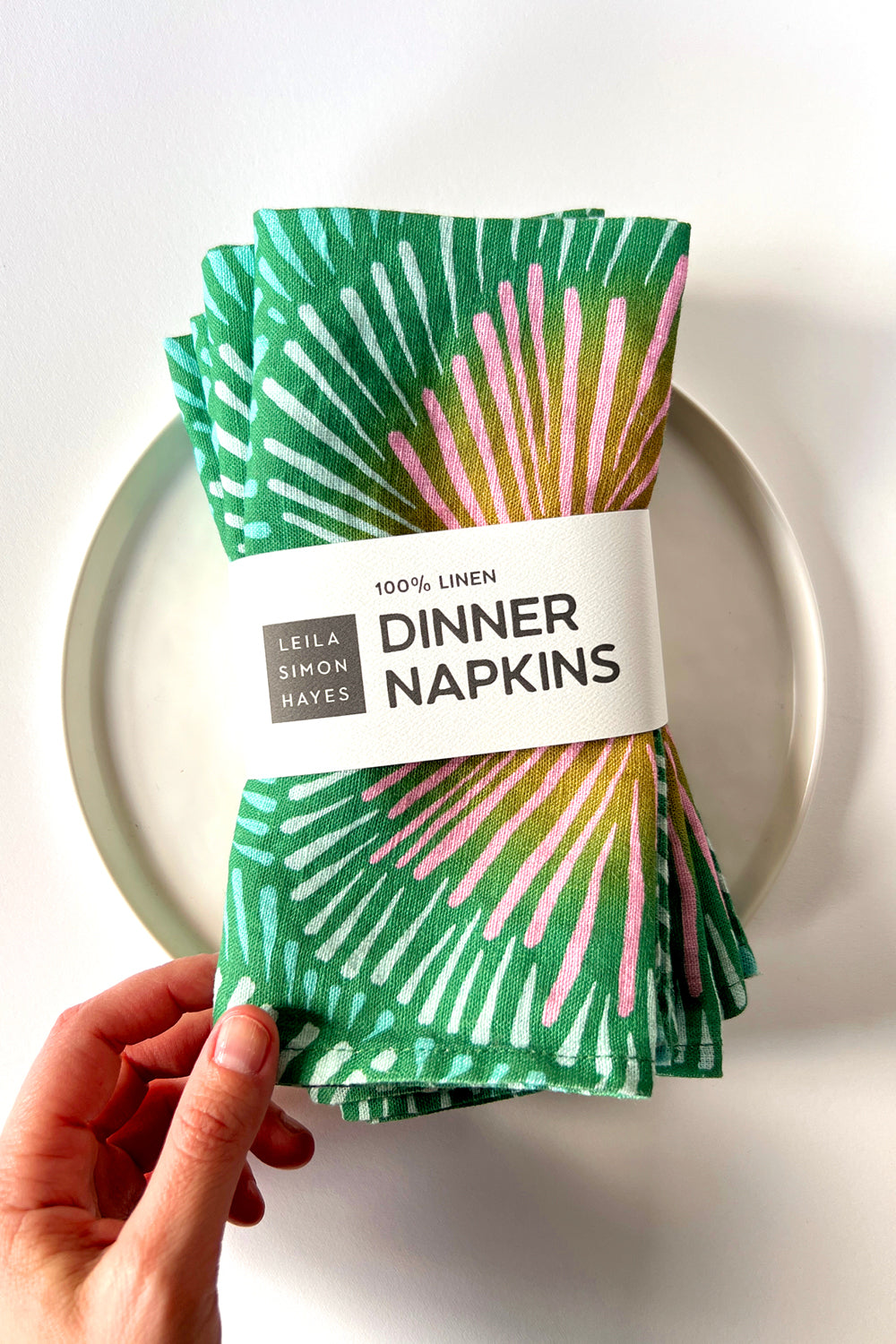 Pack of four green and pink patterned dinner napkins with a white label saying "100% Linen Dinner Napkins", designed by artist Leila Simon Hayes. 