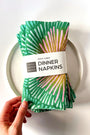 Pack of four green and pink patterned dinner napkins with a white label saying "100% Linen Dinner Napkins", designed by artist Leila Simon Hayes. 