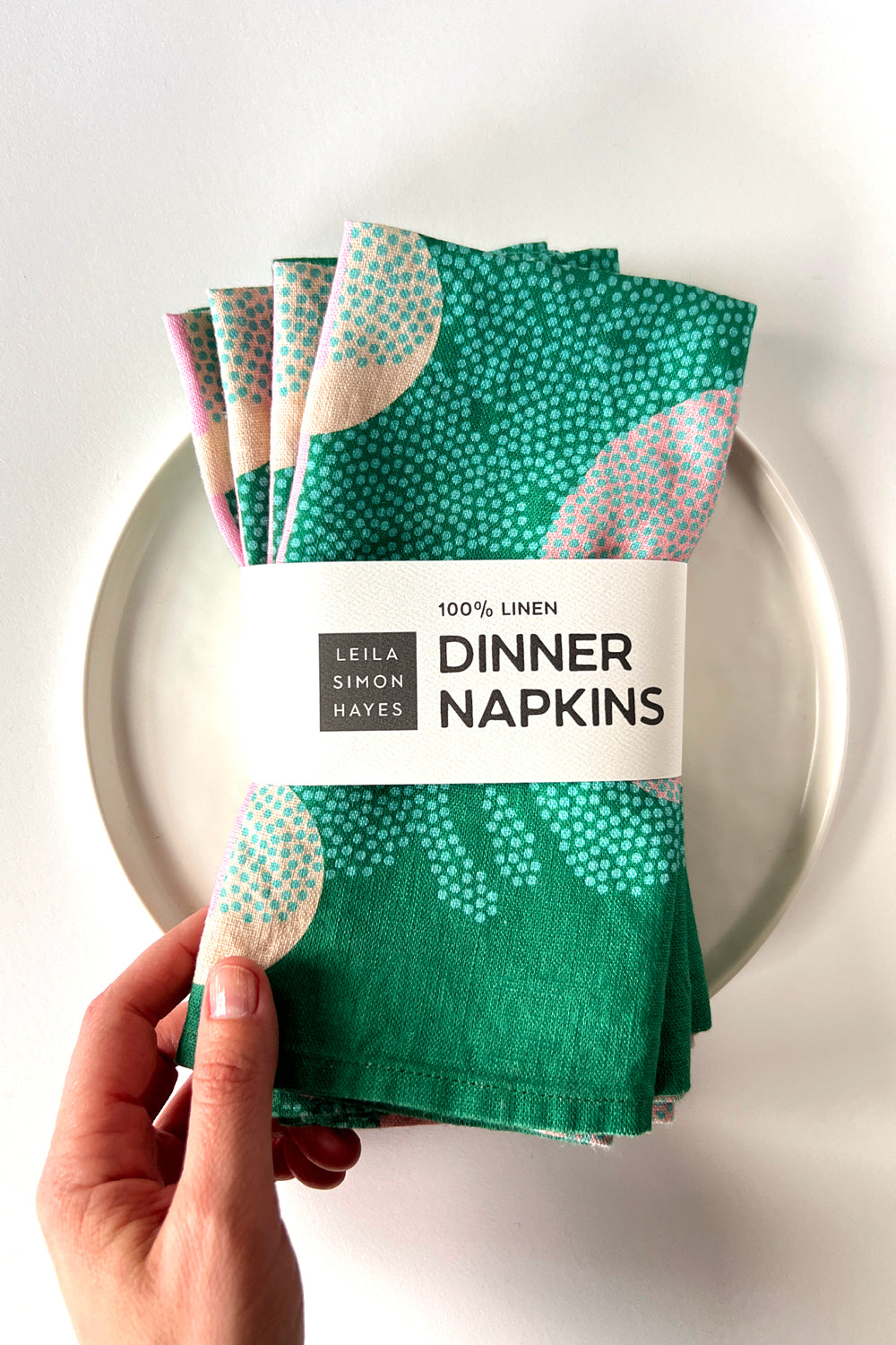 Pack of four green patterned dinner napkins with a brand label saying "100% Linen Dinner Napkins", designed by artist Leila Simon Hayes. 