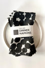 A four pack of black and white polka dot patterned dinner napkins on a white plate with a label saying "100% Linen Dinner Napkins", designed by artist Leila Simon Hayes.