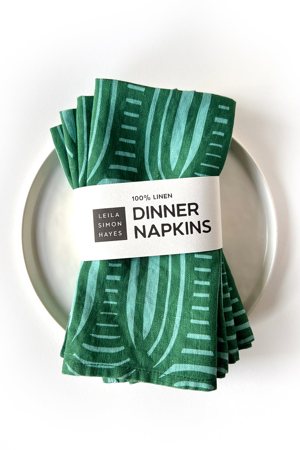 Set of 4 green patterned dinner napkins on a white plate with a label saying "100% linen Dinner Napkins", designed by artist Leila Simon Hayes