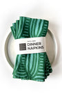 Set of 4 green patterned dinner napkins on a white plate with a label saying "100% linen Dinner Napkins", designed by artist Leila Simon Hayes