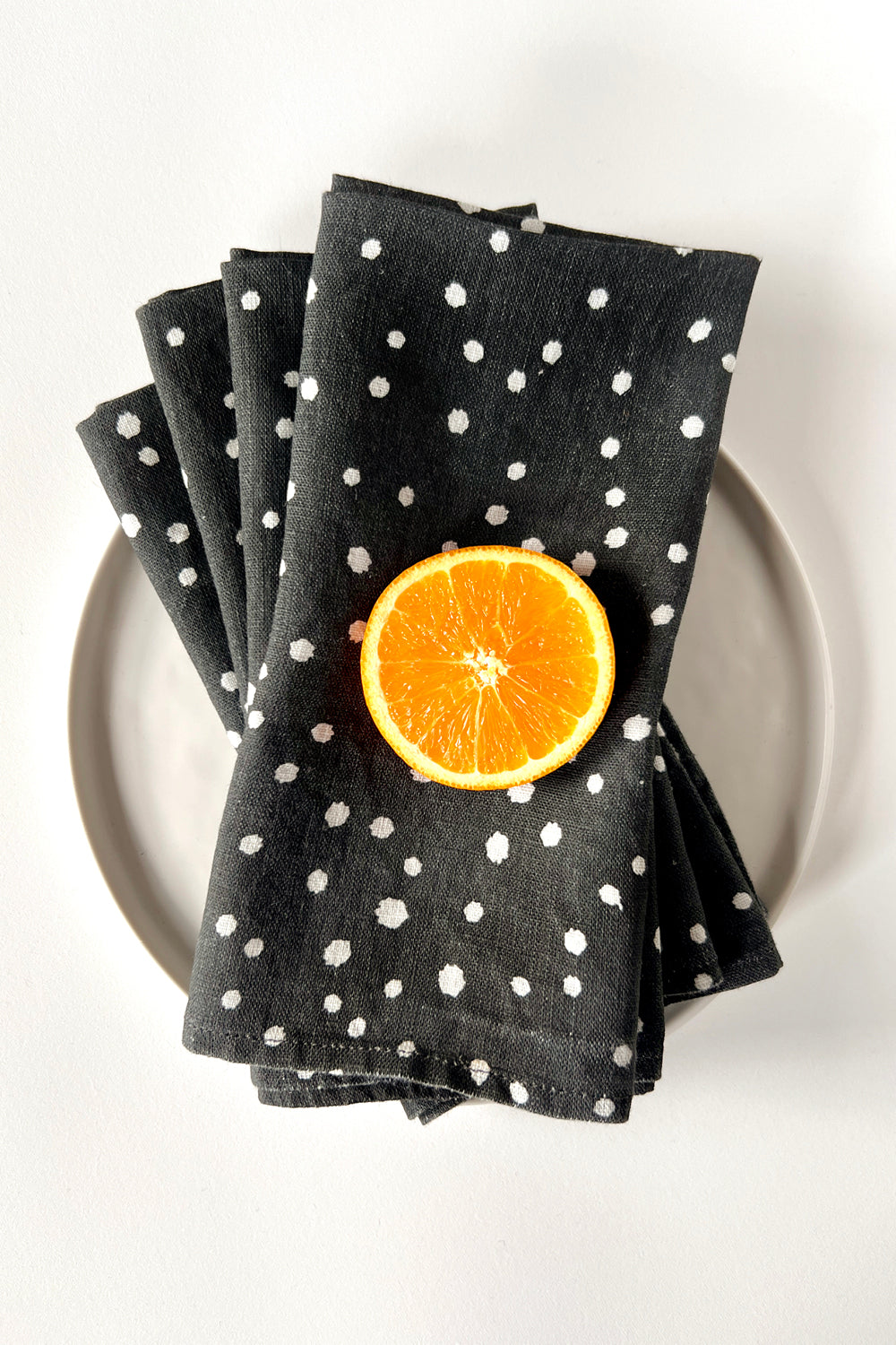 Black linen napkins with white organic polka dot shapes on a plate. Designed by artist Leila Simon Hayes