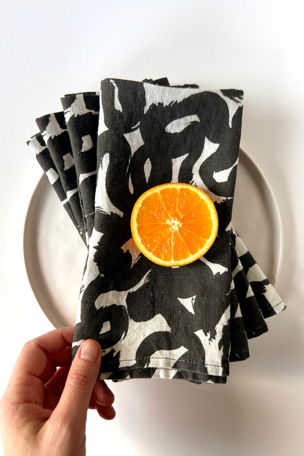 Set of four black and white patterned napkins, designed by artist Leila Simon Hayes. Napkins are layered on a white plate.