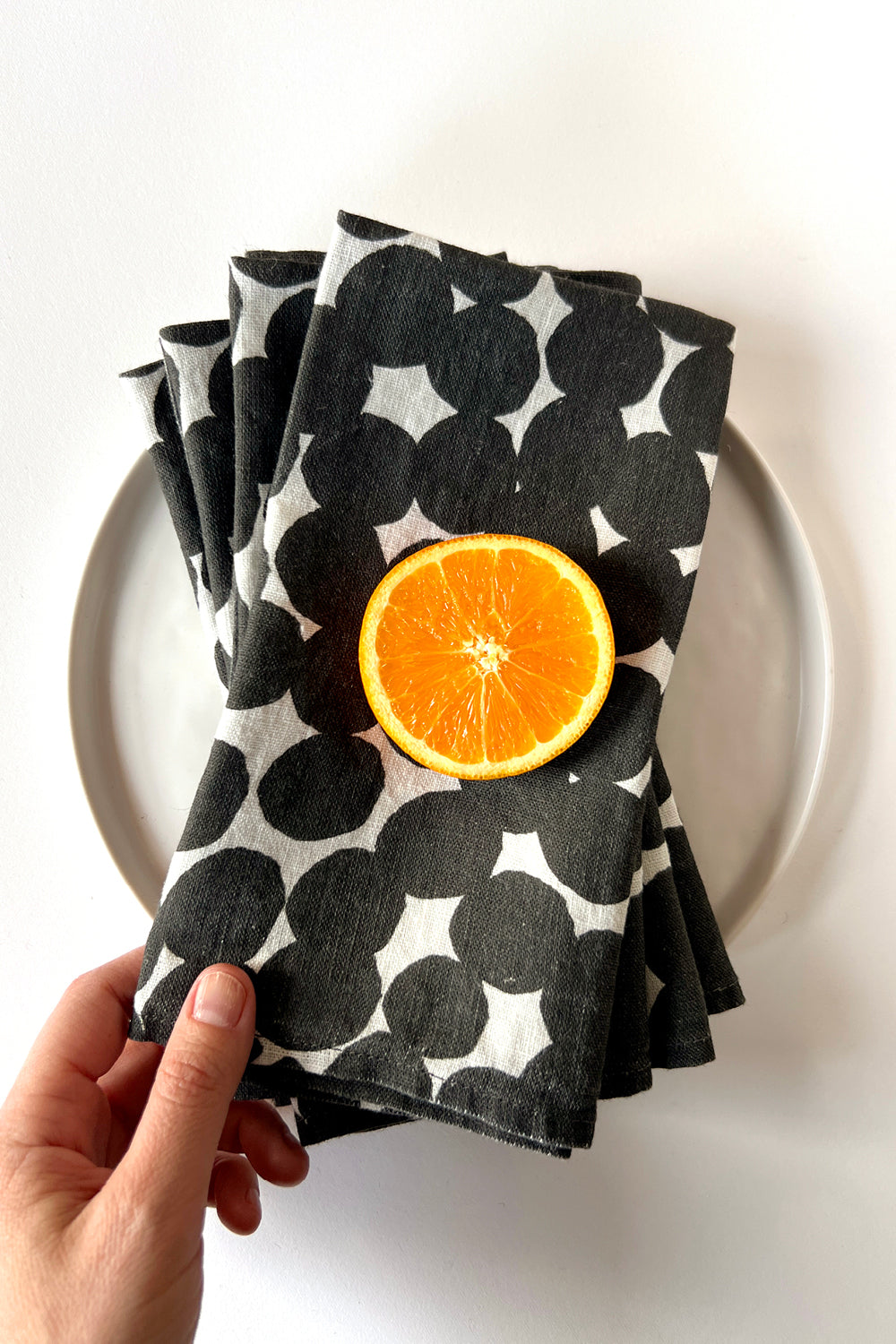 Four white linen napkins with white polka dots, designed by artist Leila Simon Hayes. Napkins are layered on a white plate.