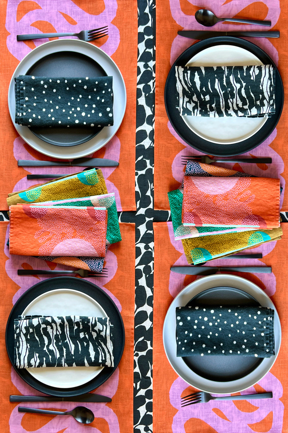 Dinner table setting with black and white variety pack of four napkins, pink and coral placemats, and black and white botanical tablecloth. Designed by artist Leila Simon Hayes.