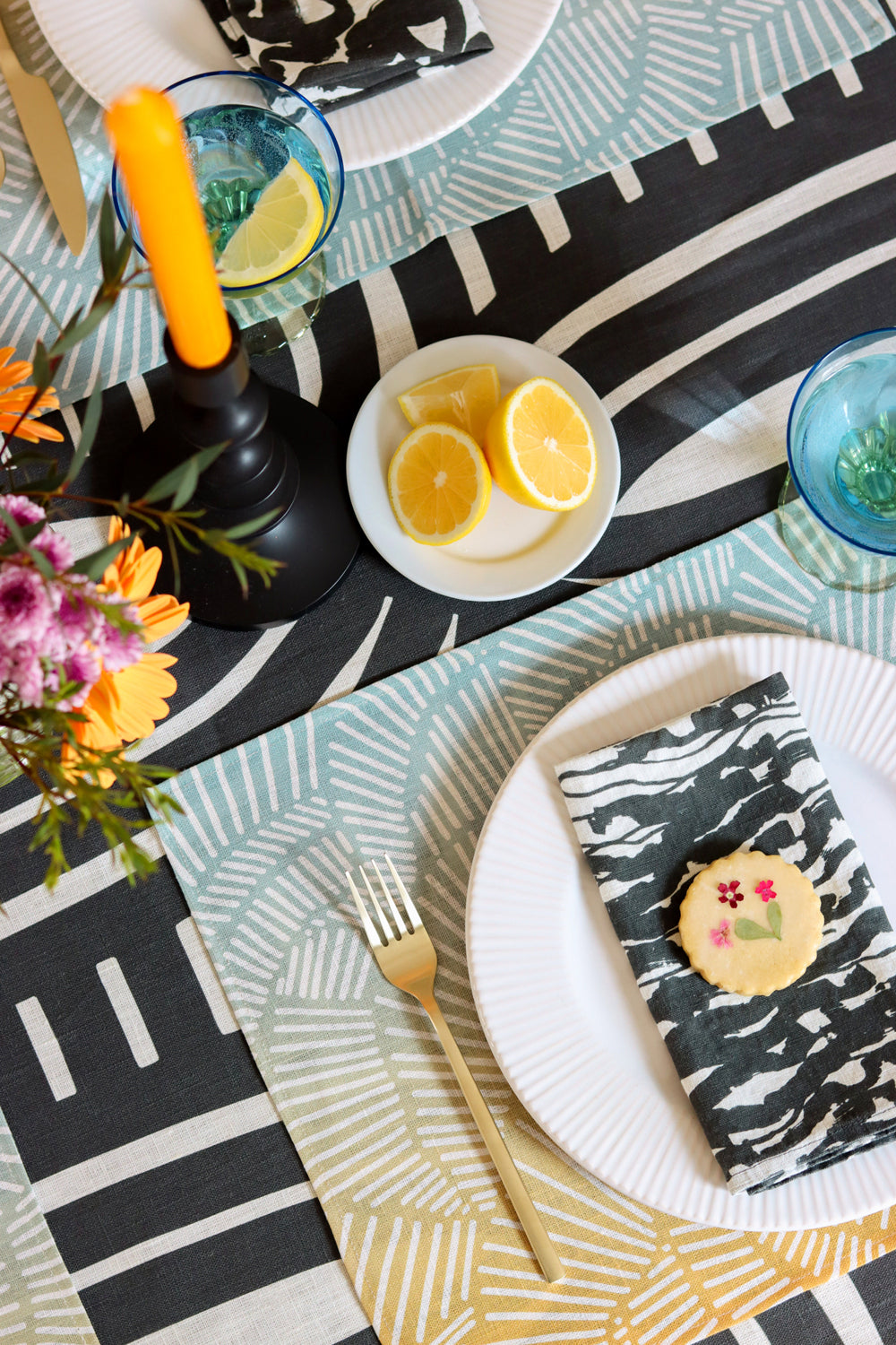 Table setting with plates, black and white wave napkins, blue and yellow placemats and a black and white stripe patterned tablecloth. Designed by artist Leila Simon Hayes.
