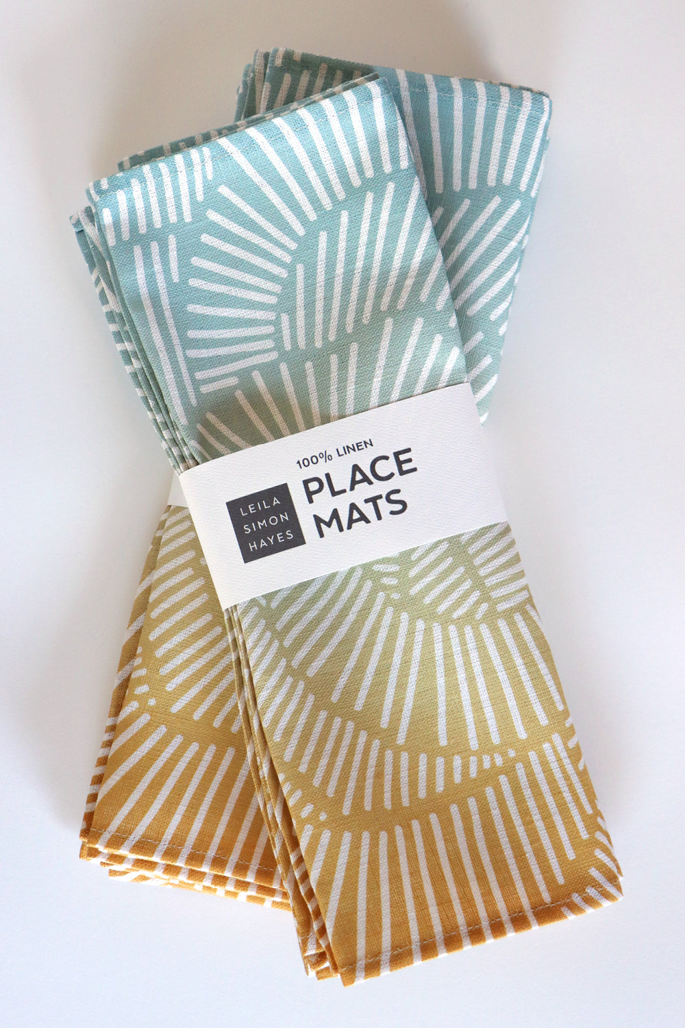Set of patterned place mats with a label saying "100% linen placemats" designed by artist Leila Simon Hayes, on a white background