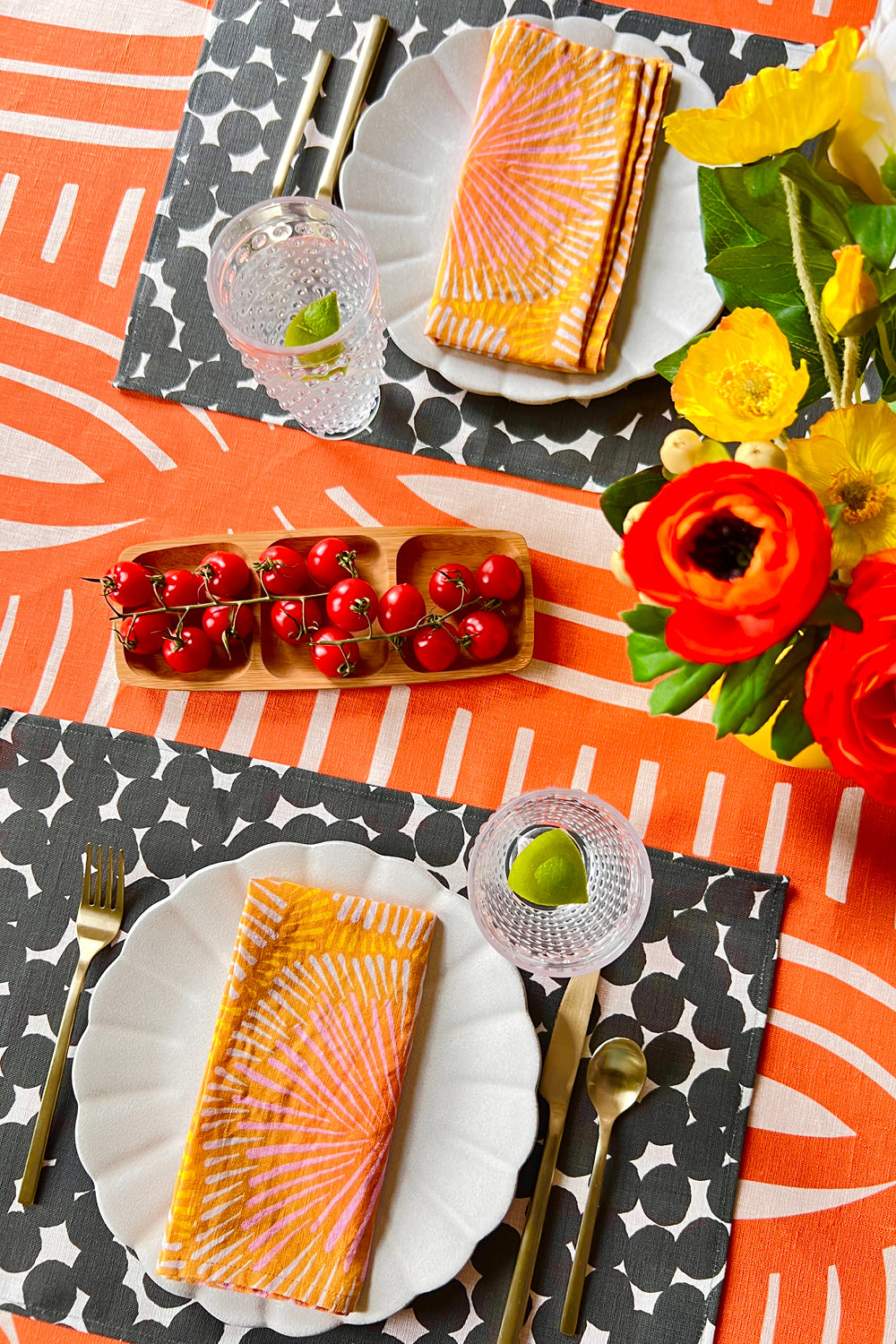 Dinner setting with orange sun burst napkins, black and white dots placemats, and a coral striped tablecloth. Designed by artist Leila Simon Hayes. 