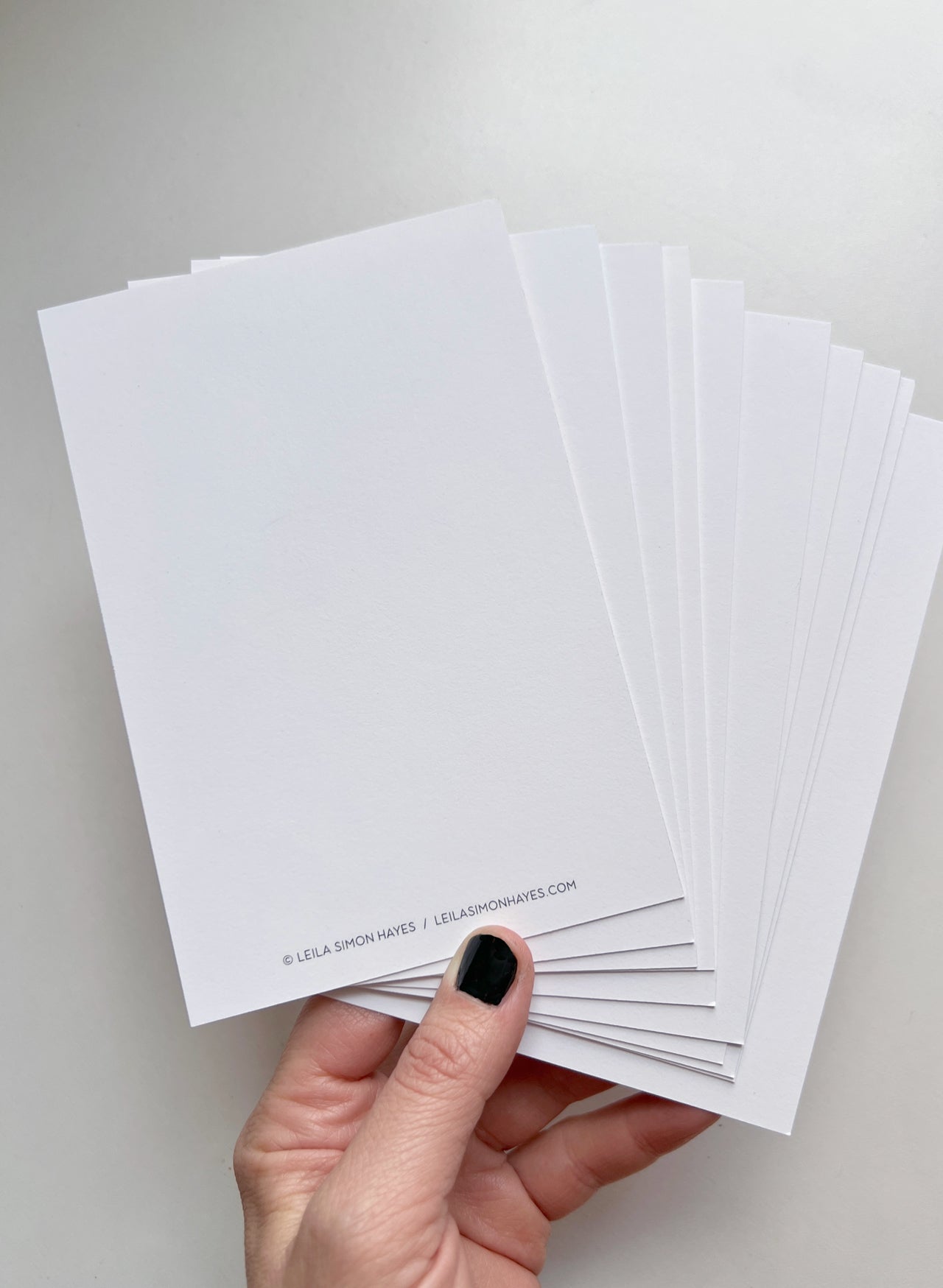 A hand holding up the back of the postcards which is blank postcards. Designed by artist Leila Simon Hayes.