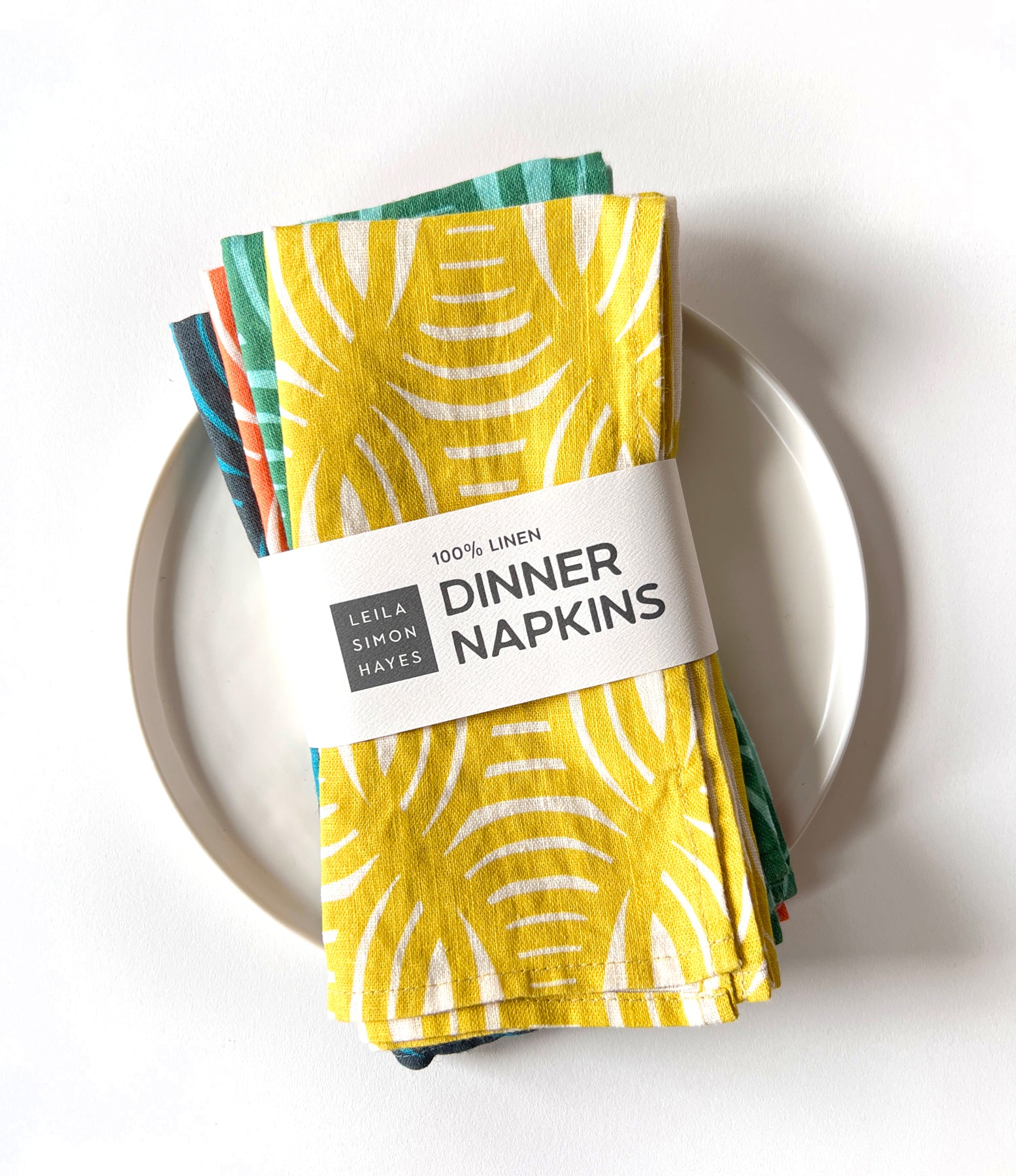 A pack of four geometrical patterned linen napkins warpped in a label saying "100% Linen Dinner Napkins" designed by artist Leila Simon Hayes