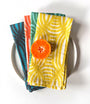 Four layered dinner napkins with a geometric pattern. Each napkin is a different color, yellow, green, blue and coral. Designed by artist Leila Simon Hayes