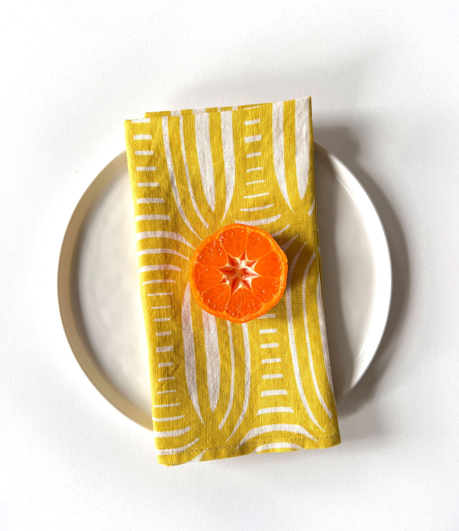 Yellow and white linen dinner napkins with unique stripe pattern with a cut orange. Designed by artist Leila Simon Hayes