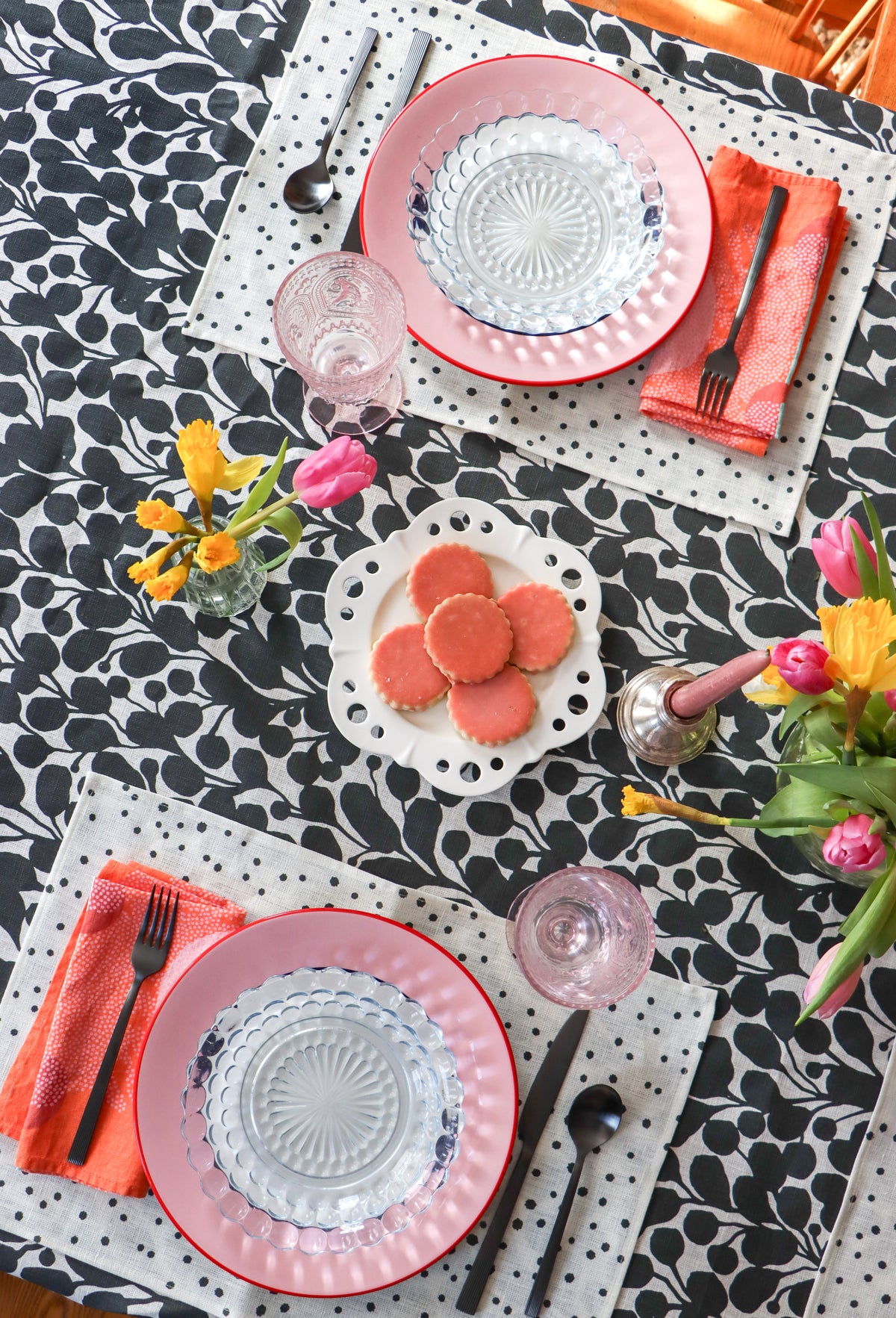 Layered black and white table linens on a dining room table set for a meal. Red napkins, white placemats with black organic dots, and a botanical black and white tablecloth, designed by artist Leila Simon Hayes