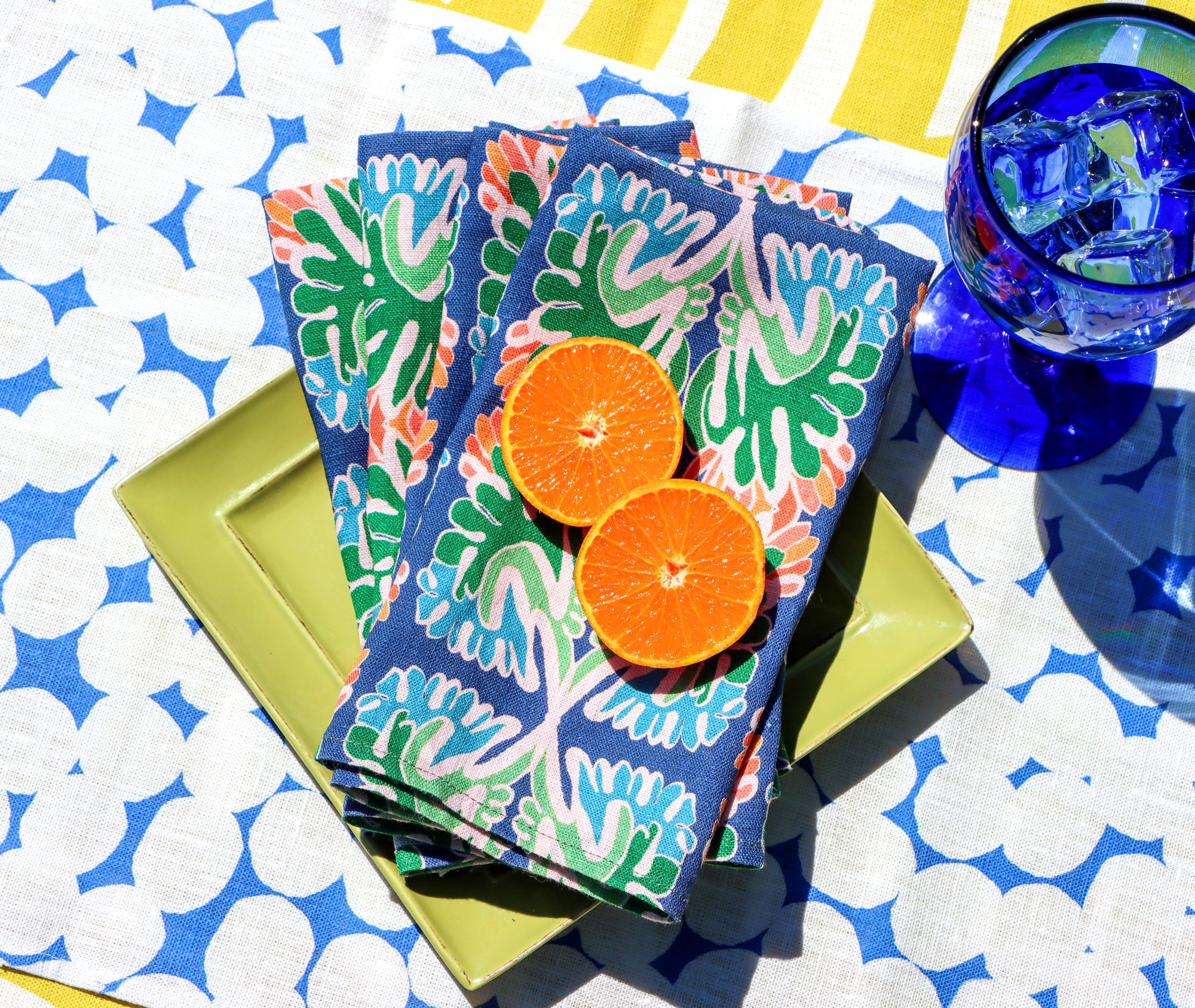 Colorful patterned napkins with orange slices on a polka dot placemat and striped tablecloth.